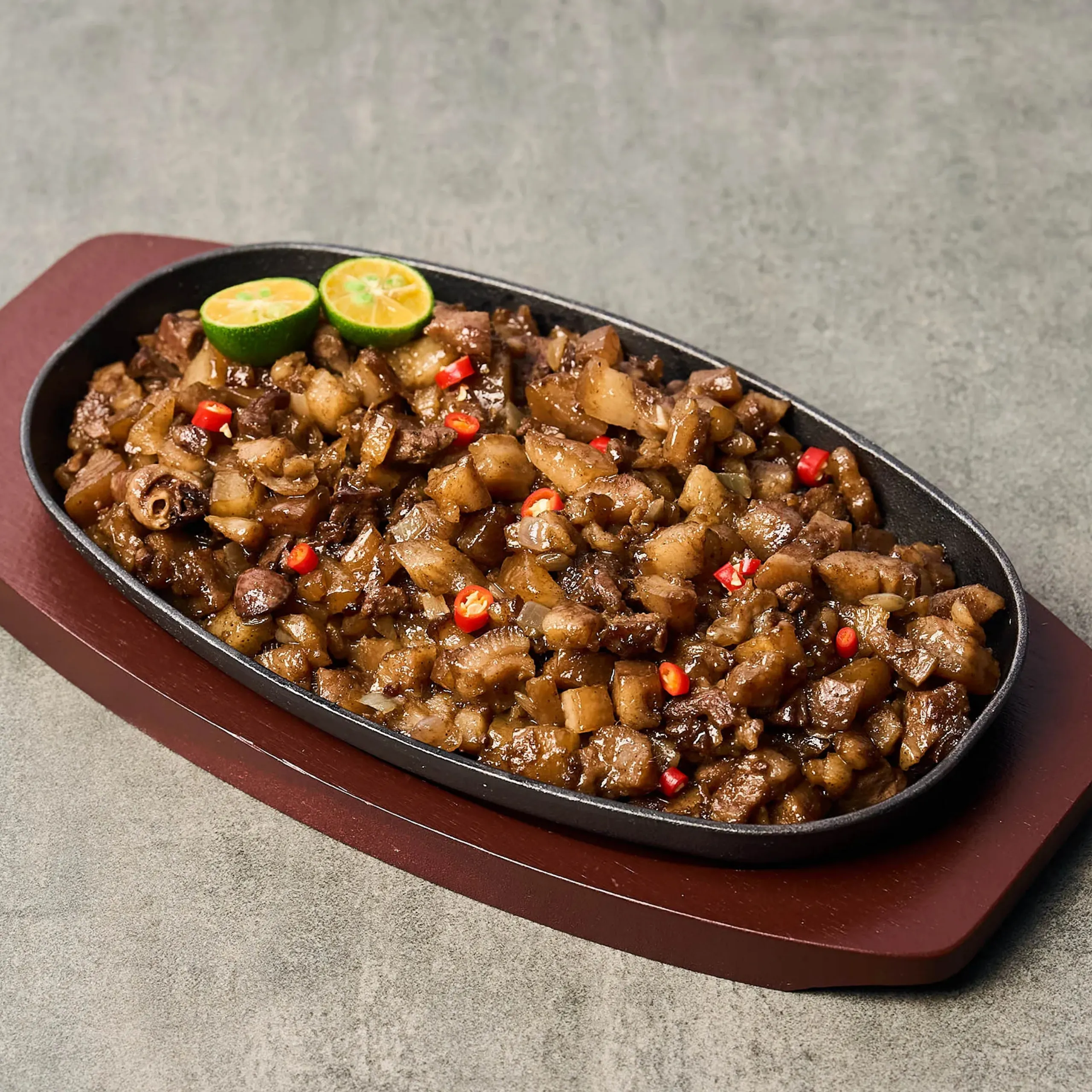 Cast-iron skillet filled with sautéed diced beef, onions, and peppers, topped with lime wedges as garnish