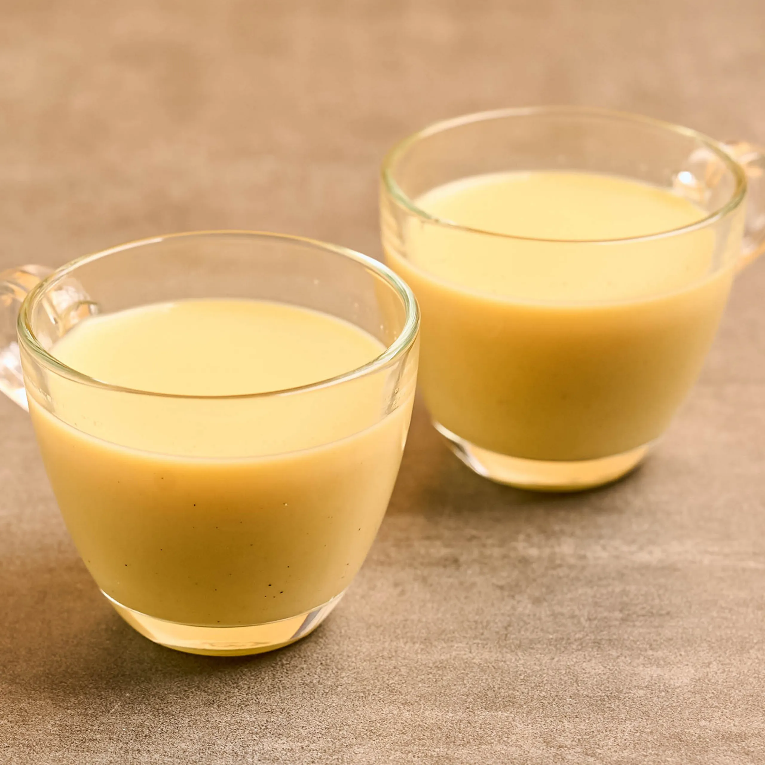 Three glass mugs filled with pale yellow juice on a gray countertop, partially visible in a close-up.