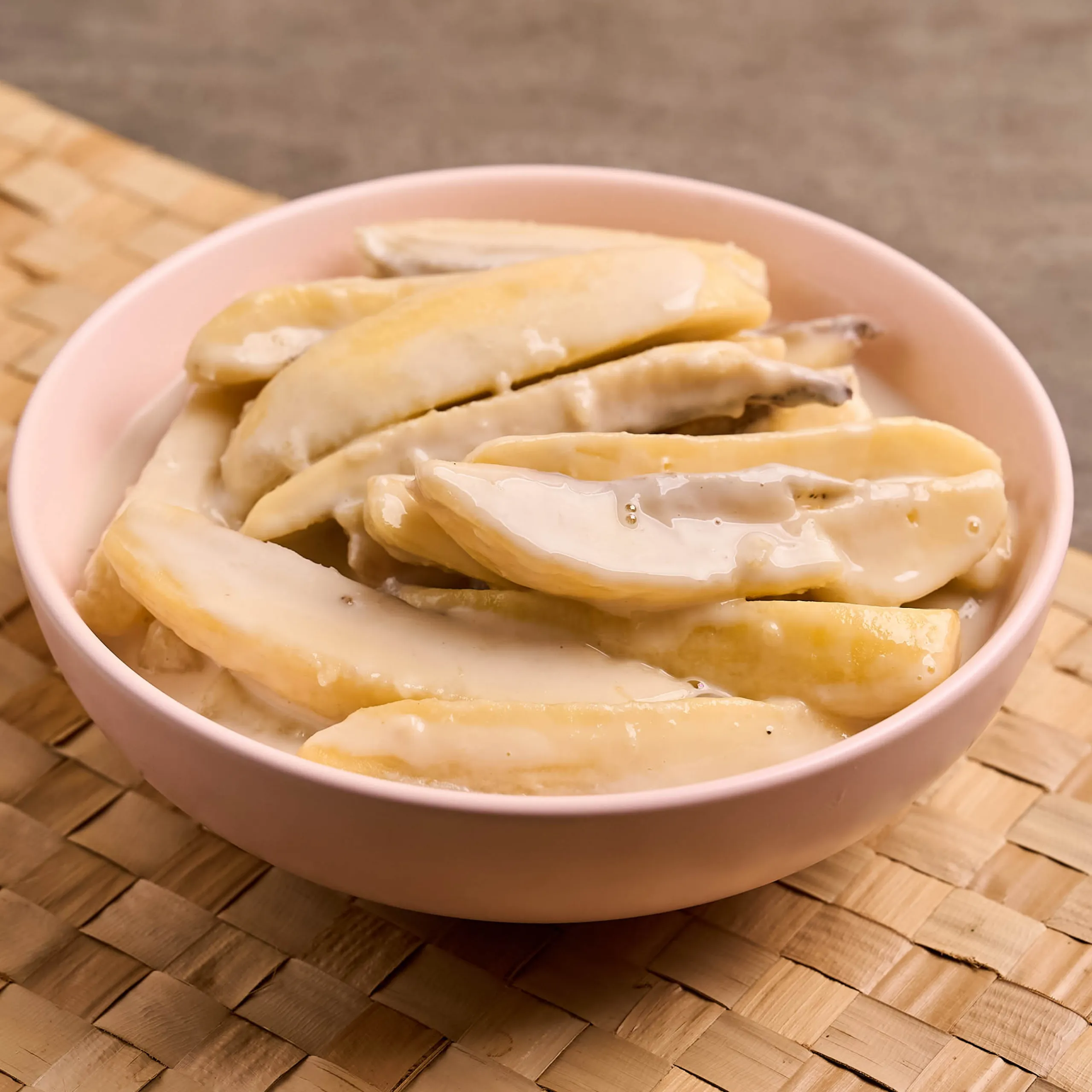 Pink bowl filled with pale dumplings arranged in a stack on a wooden surface.