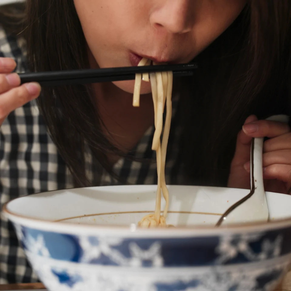 a woman slurping a warm bowl of savory ramen with borth and noodles