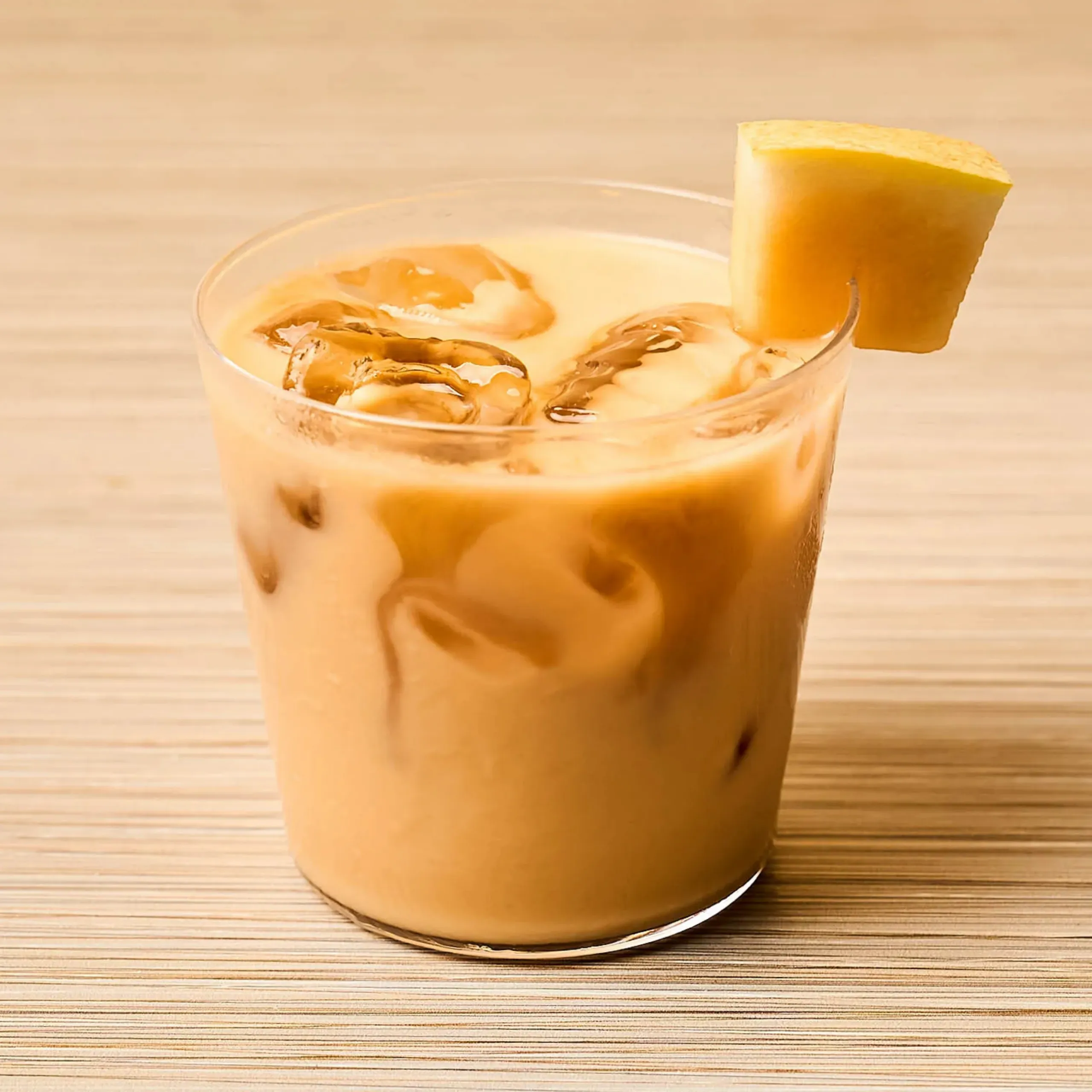 Close-up of an iced coffee in a tall glass with ice cubes and a lemon wedge garnish on the rim, set on a wooden surface.
