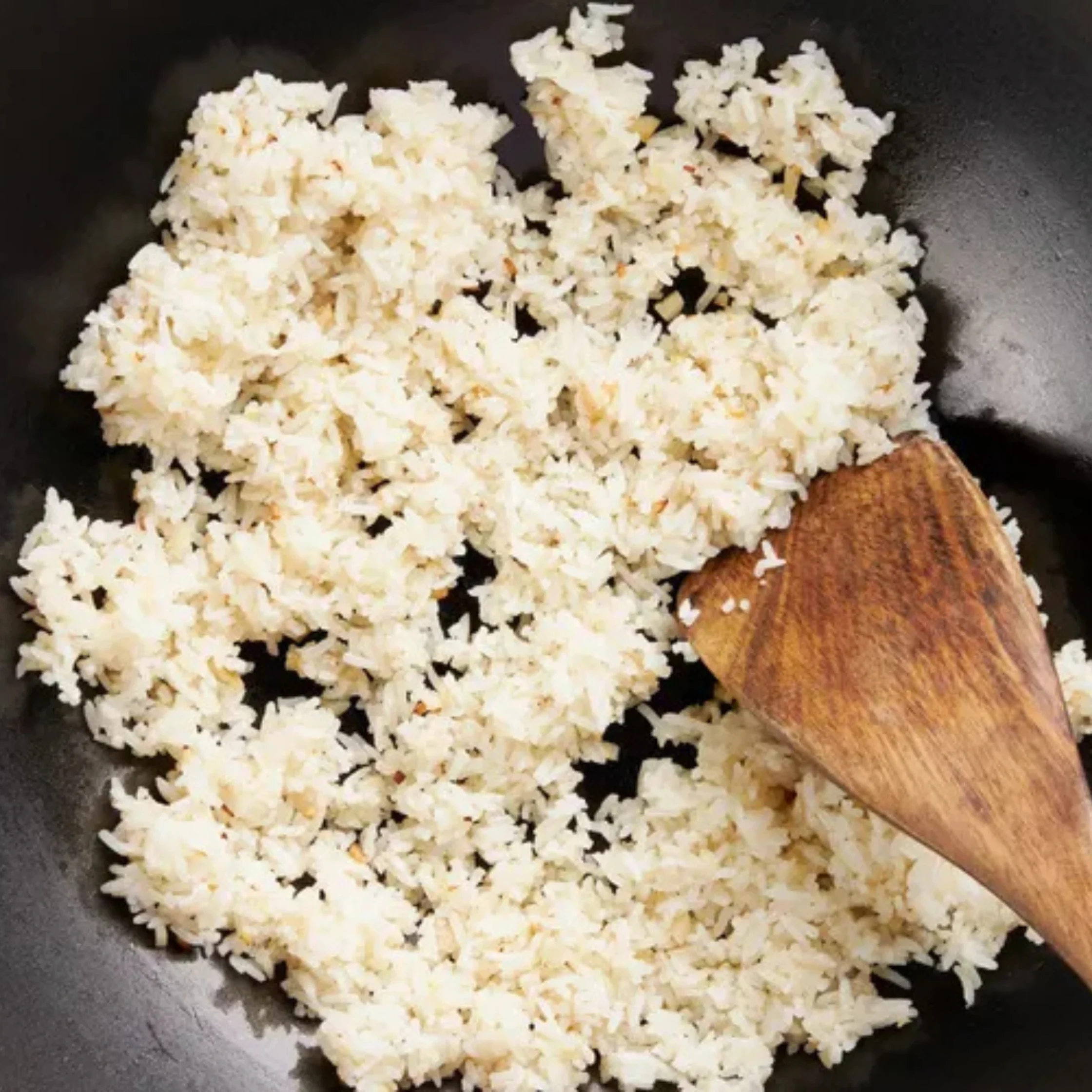 wooden spoon mixing garlic rice in a pan