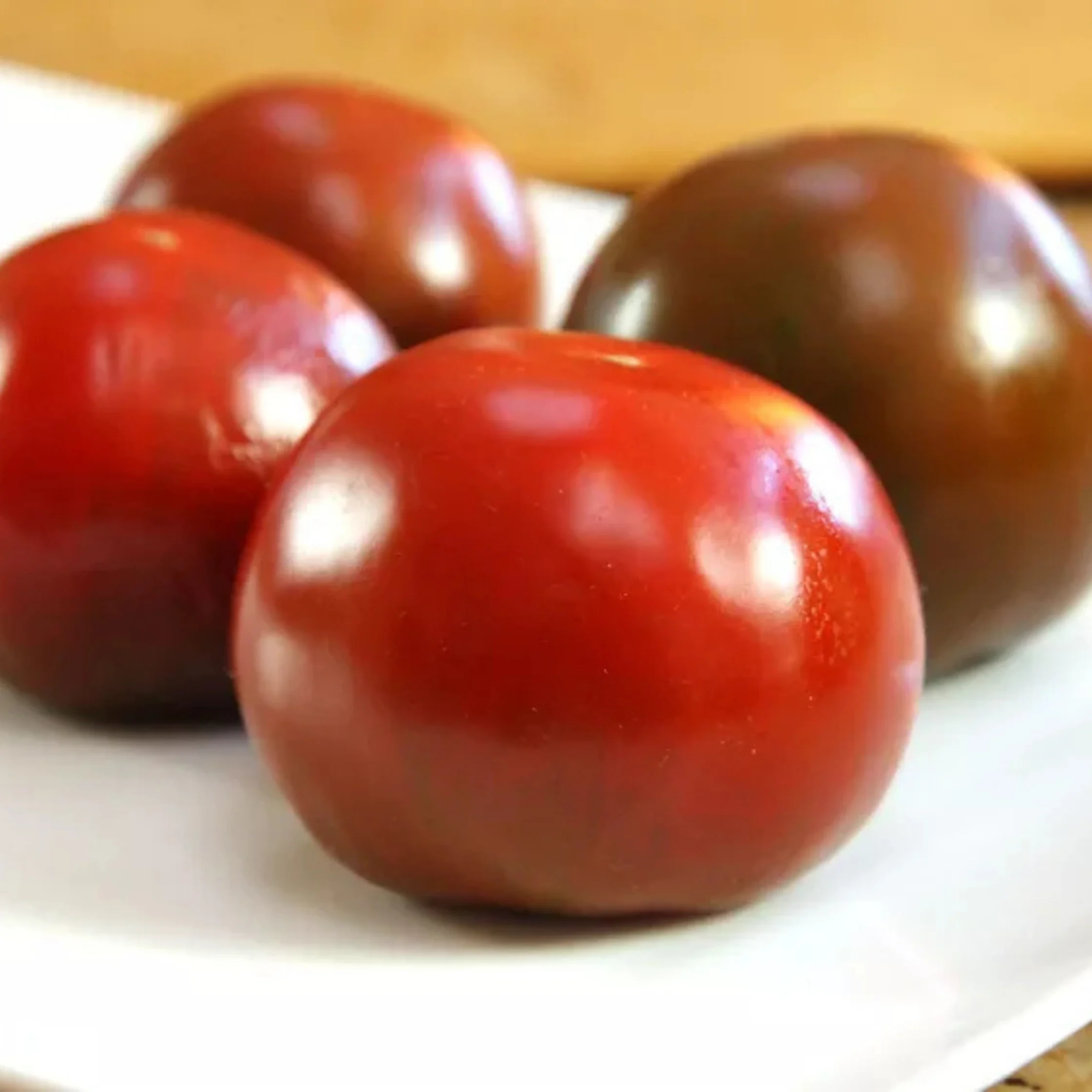 four tomatoes all placed stem side down on a white plate on a brown table