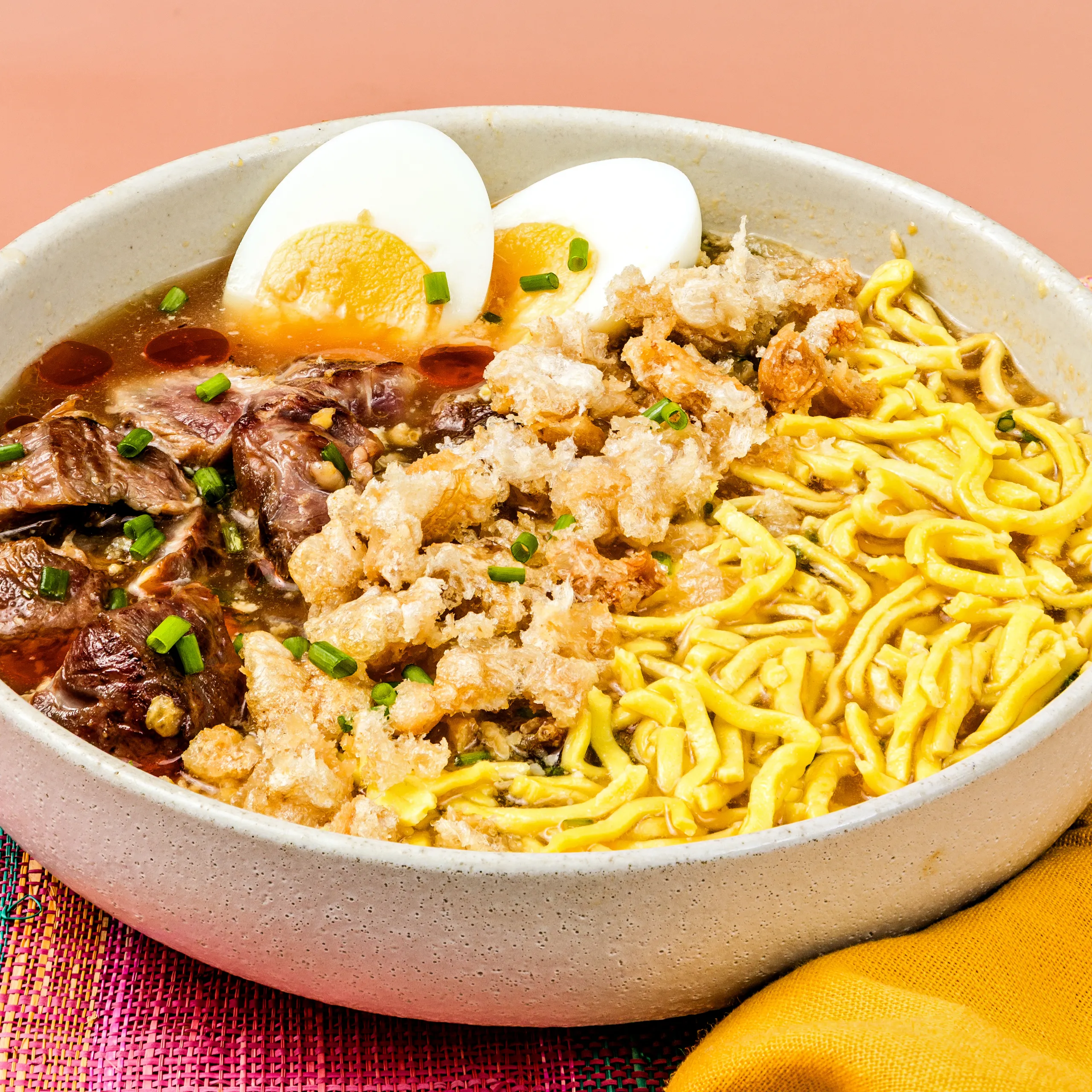 Noodle soup (ramen) bowl with half a boiled egg, beef slices, green onions, crispy fried pieces, and broth.