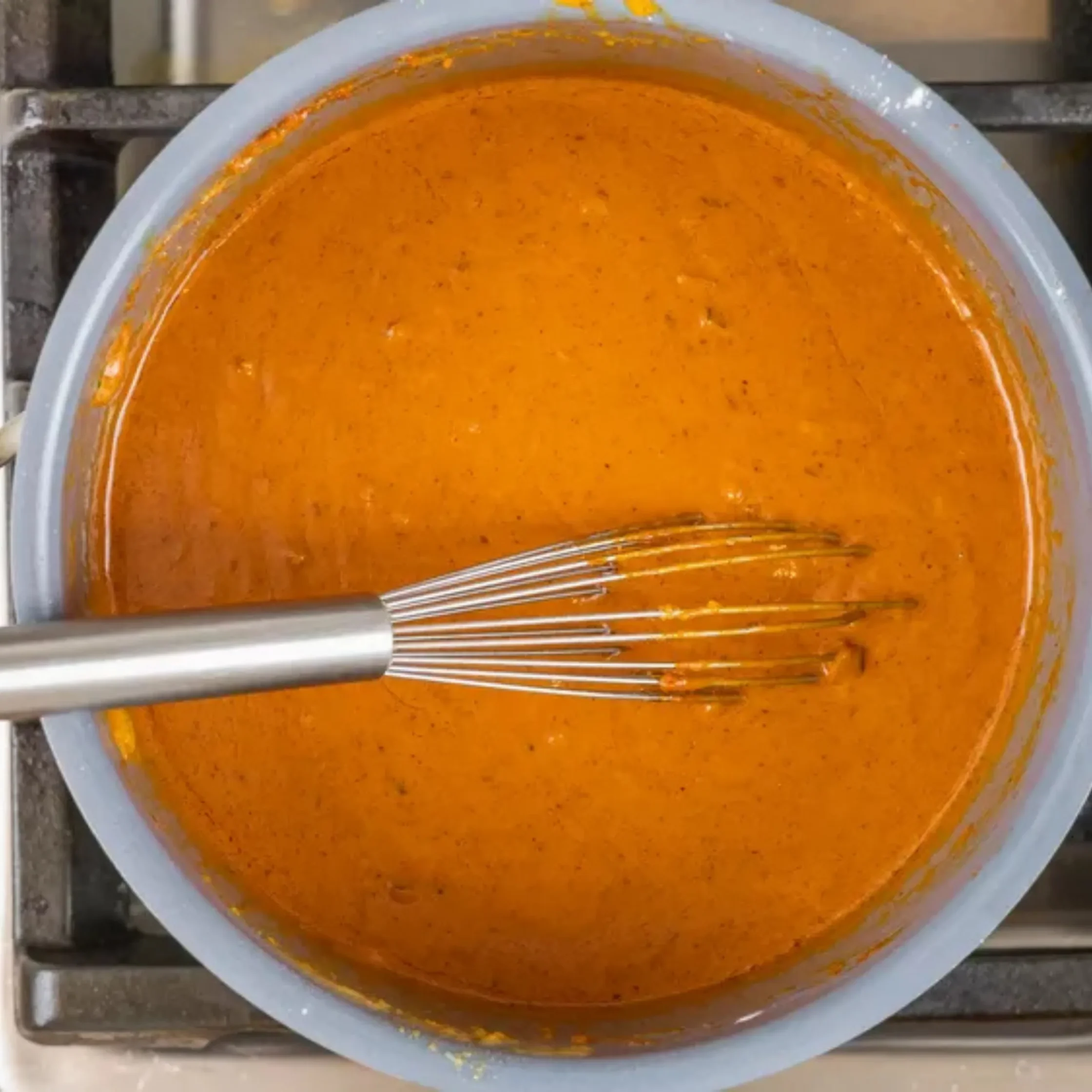 orange sauce kare-kare in a grey pan with a whisk mixing int
