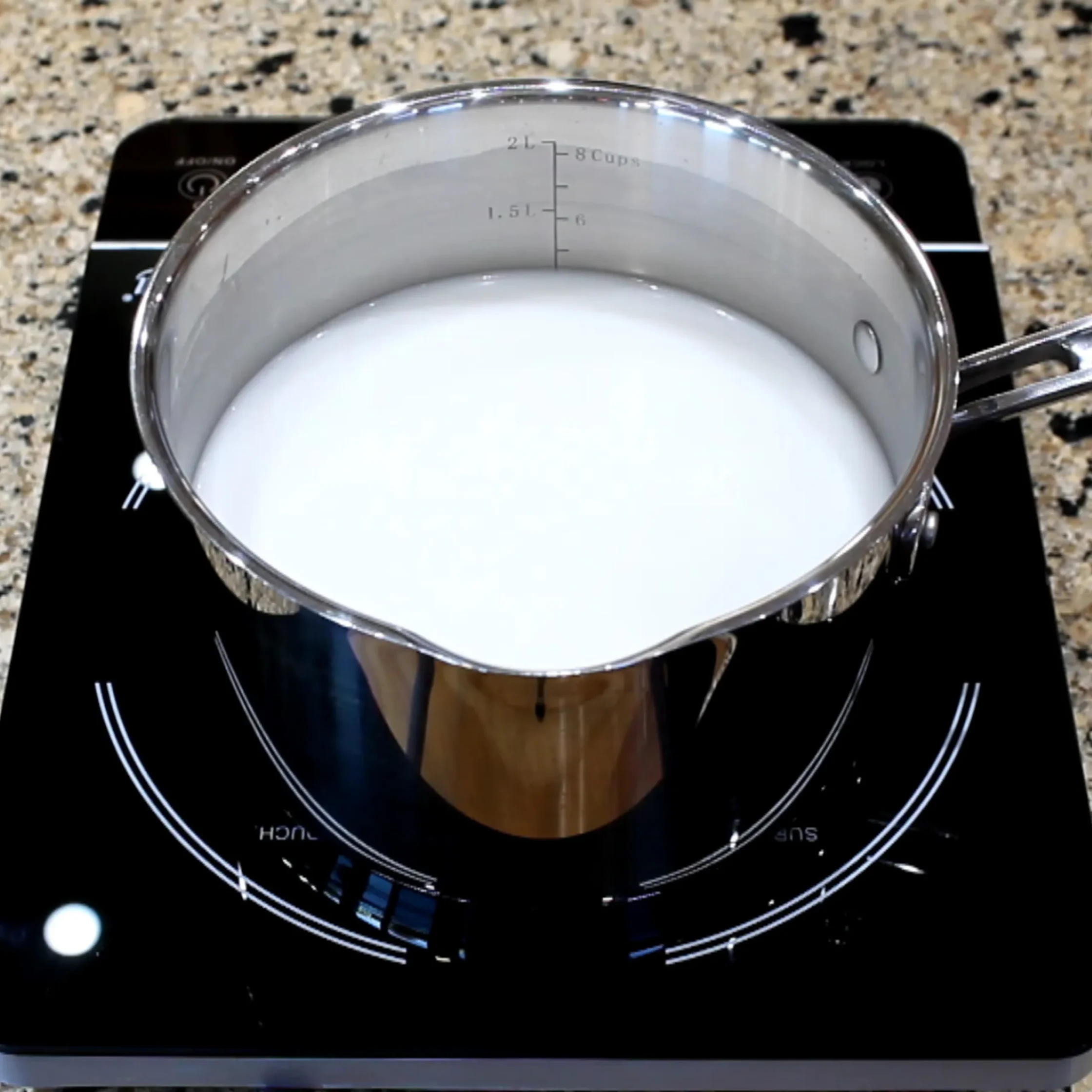 silver metal pot filled with white liquie coconut milk on a black induction stove on a marble counter