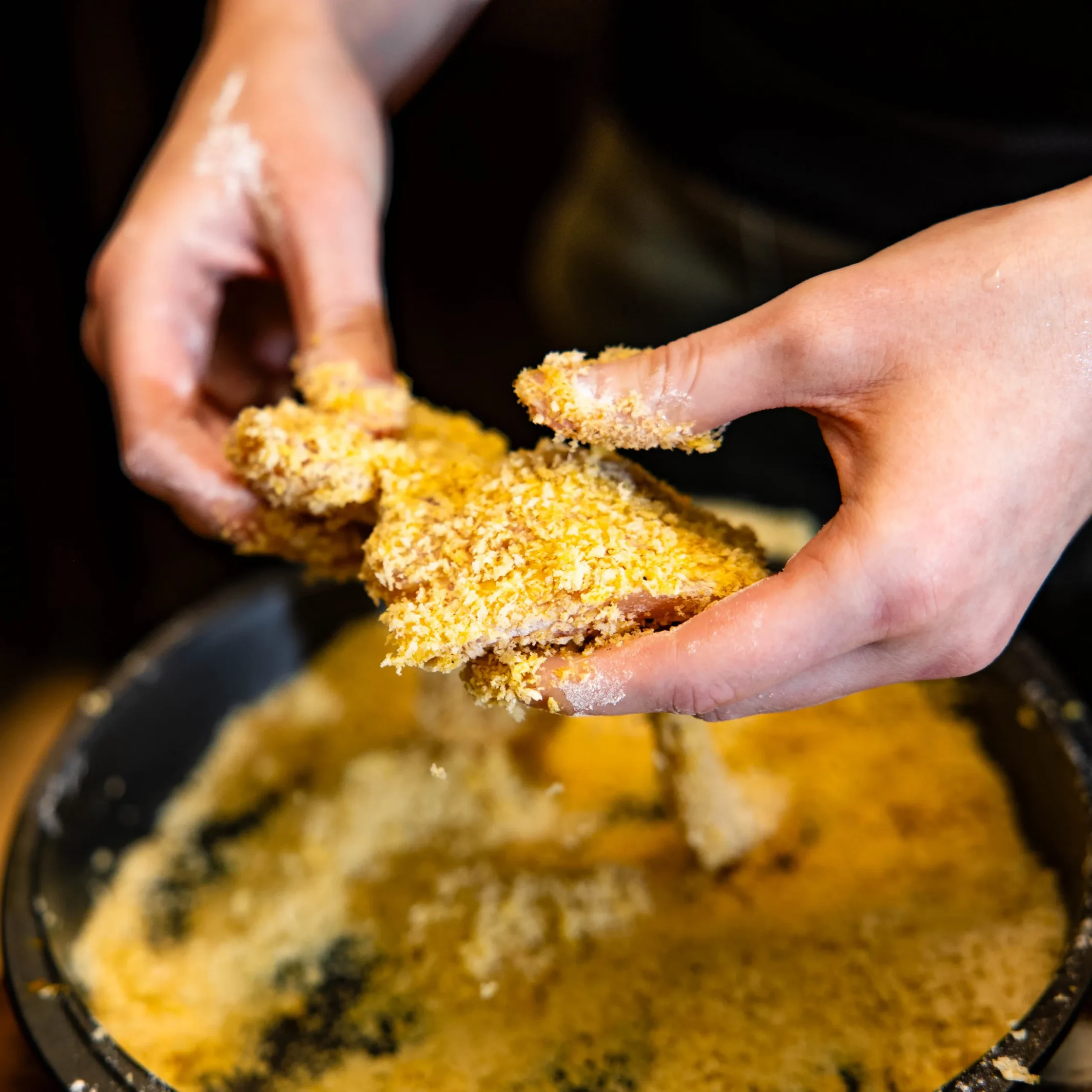 Close-up of hands tearing apart crumbly dough in a mixing bowl, with yellow-crumb colorings visible.