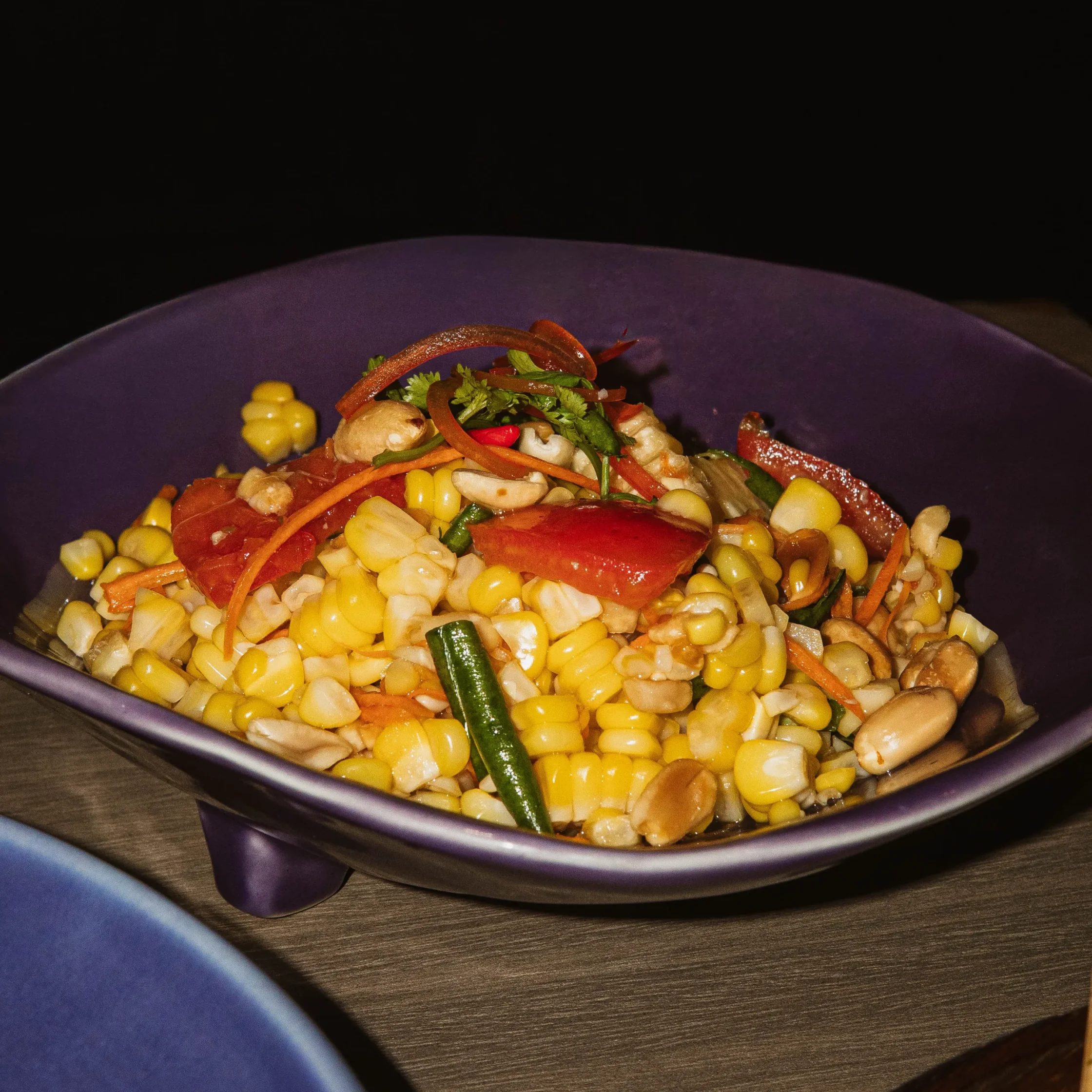Close-up of a colorful vegetable corn salad in a purple bowl, showing corn kernels, diced peppers, and chopped herbs.