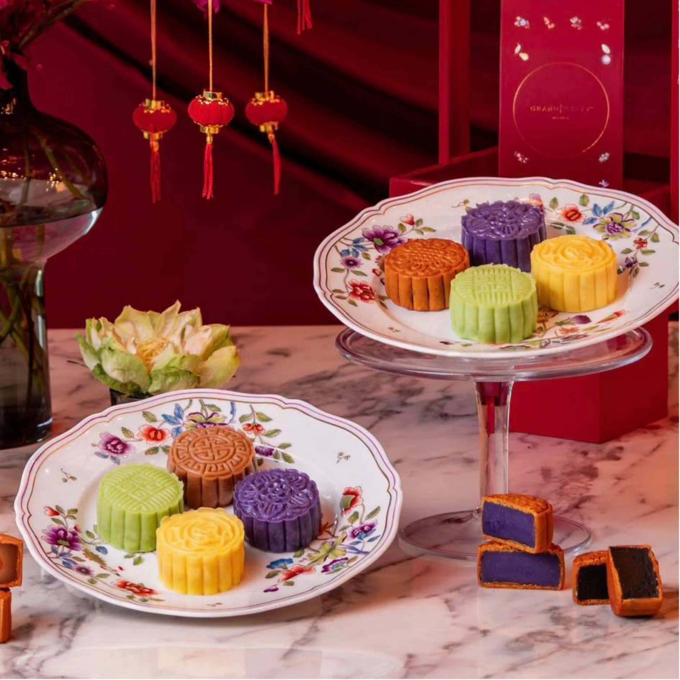 Colorful Chinese mooncakes in floral dishes, surrounded by tea, lanterns, and red décor, creating a festive, elegant Mid-Autumn mood.
