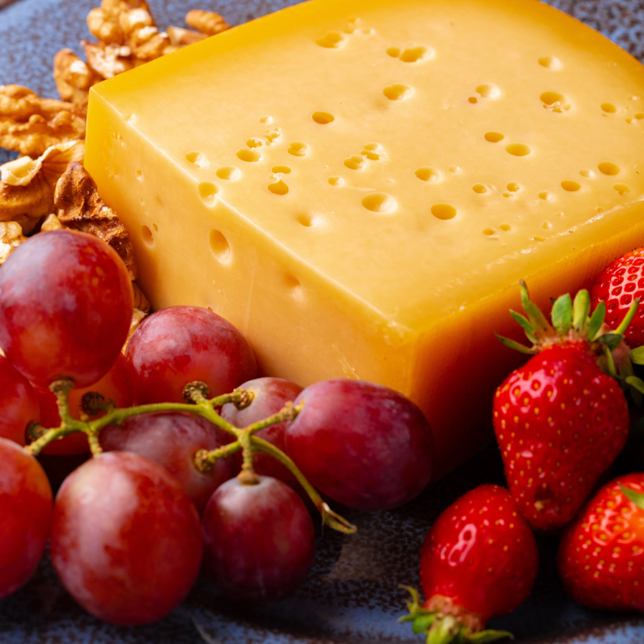 block of cheese with holes, served grapes and strawberries on a grey plate