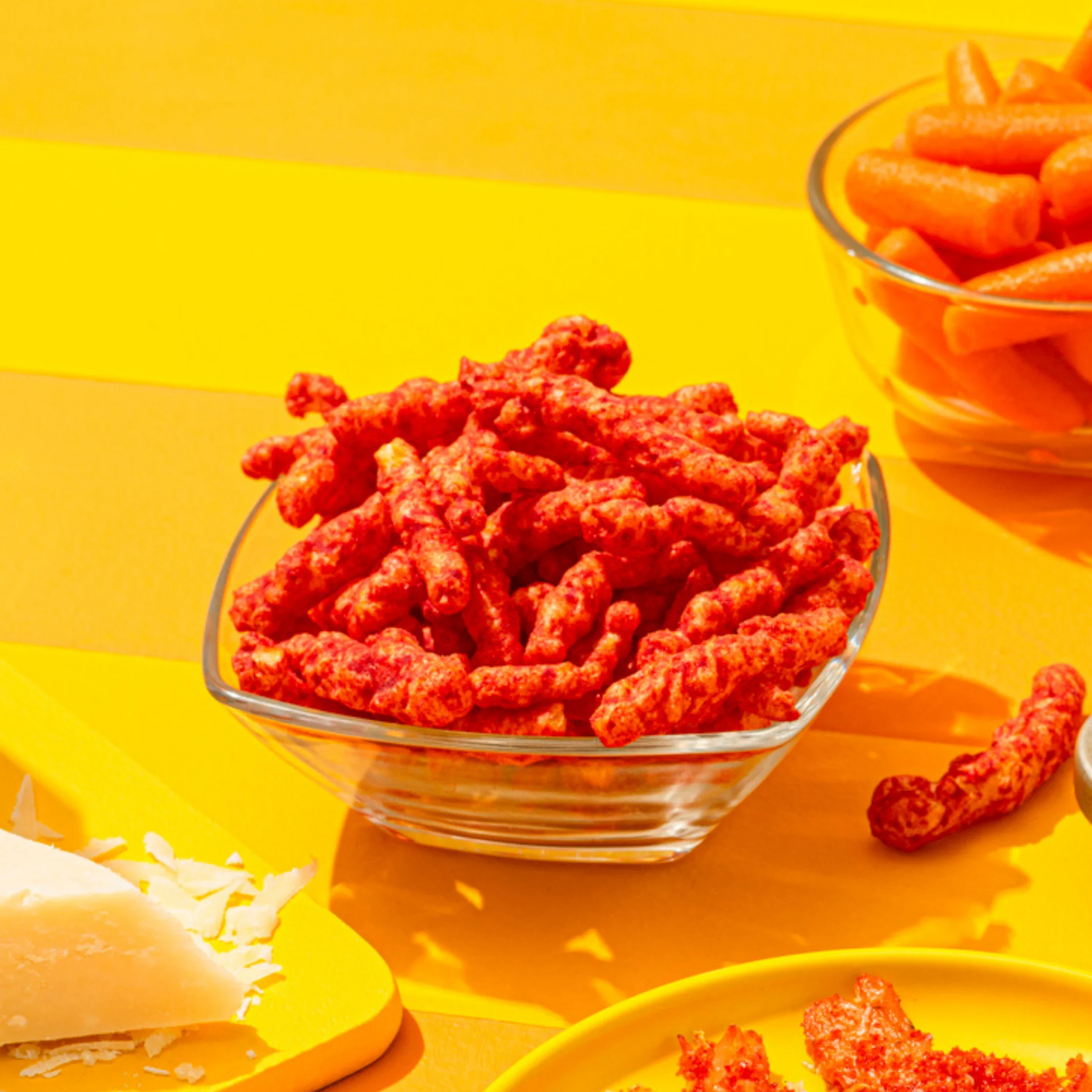 pieces of cheetos in a small glass bowl on a yellow surface