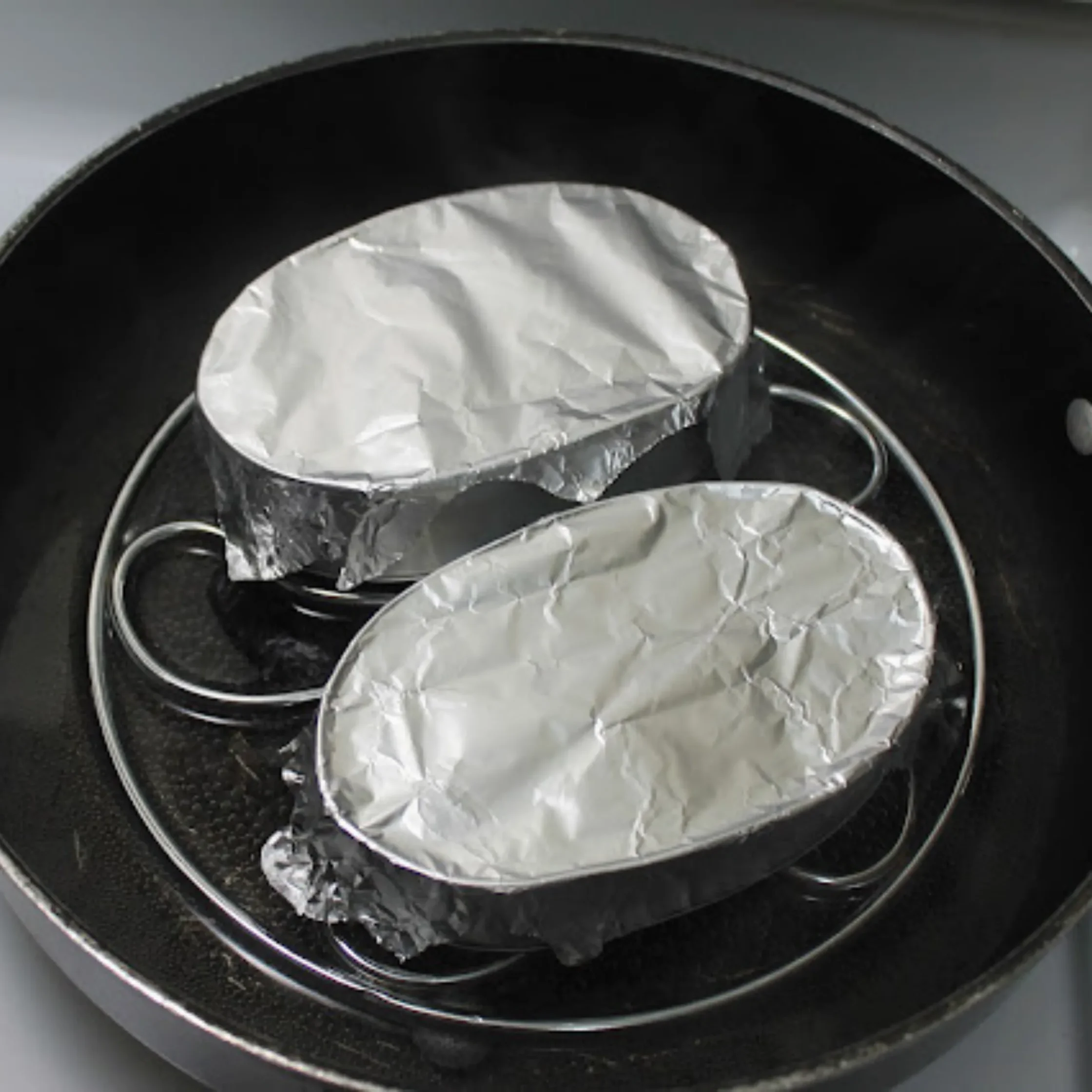 Close-up of foil-wrapped packets placed in a dark round pan or pot, ready for cooking.