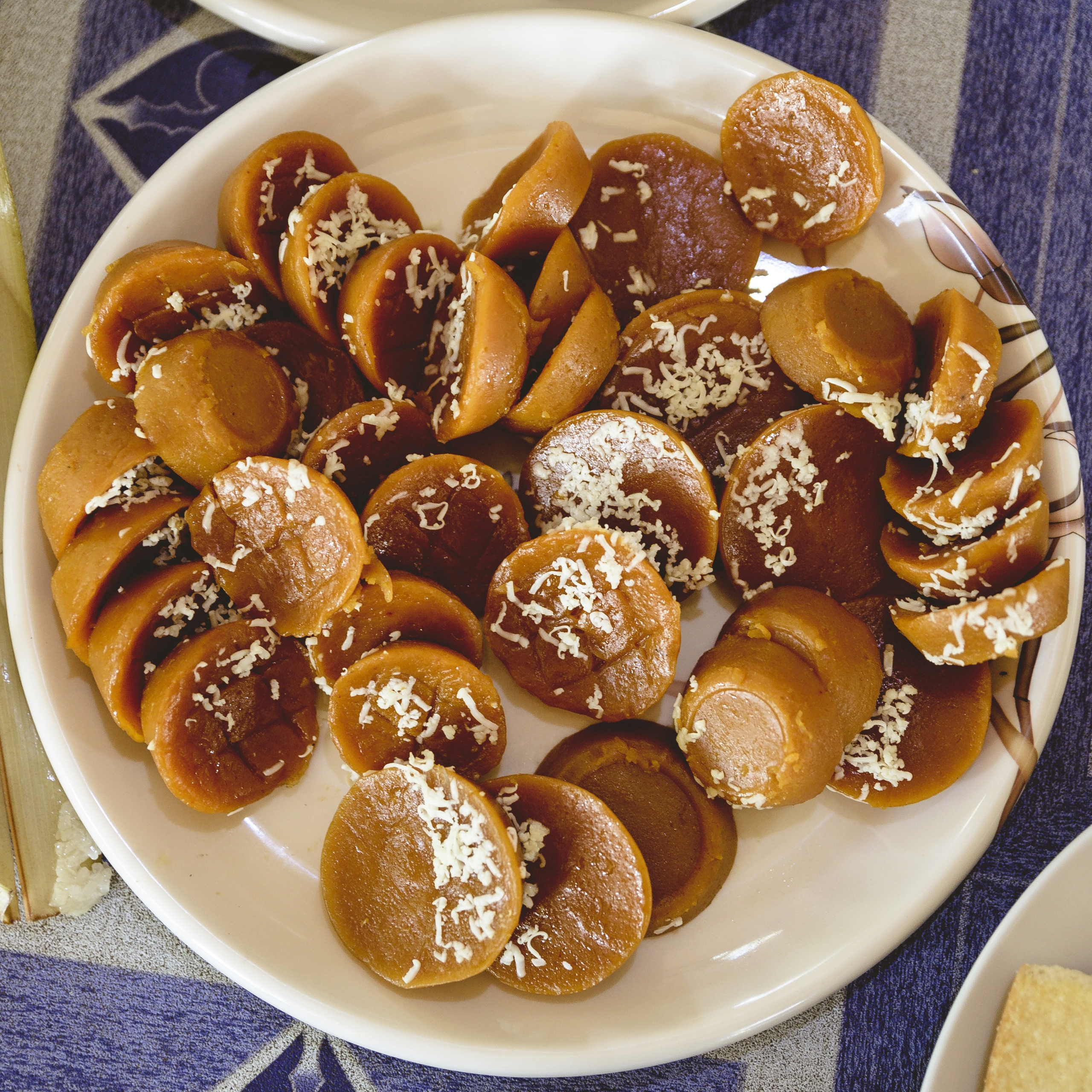 Overhead view of a white platter piled with glossy golden-brown mini pancakes, some folded, and sprinkled with shredded coconut; a warm, festive dessert.