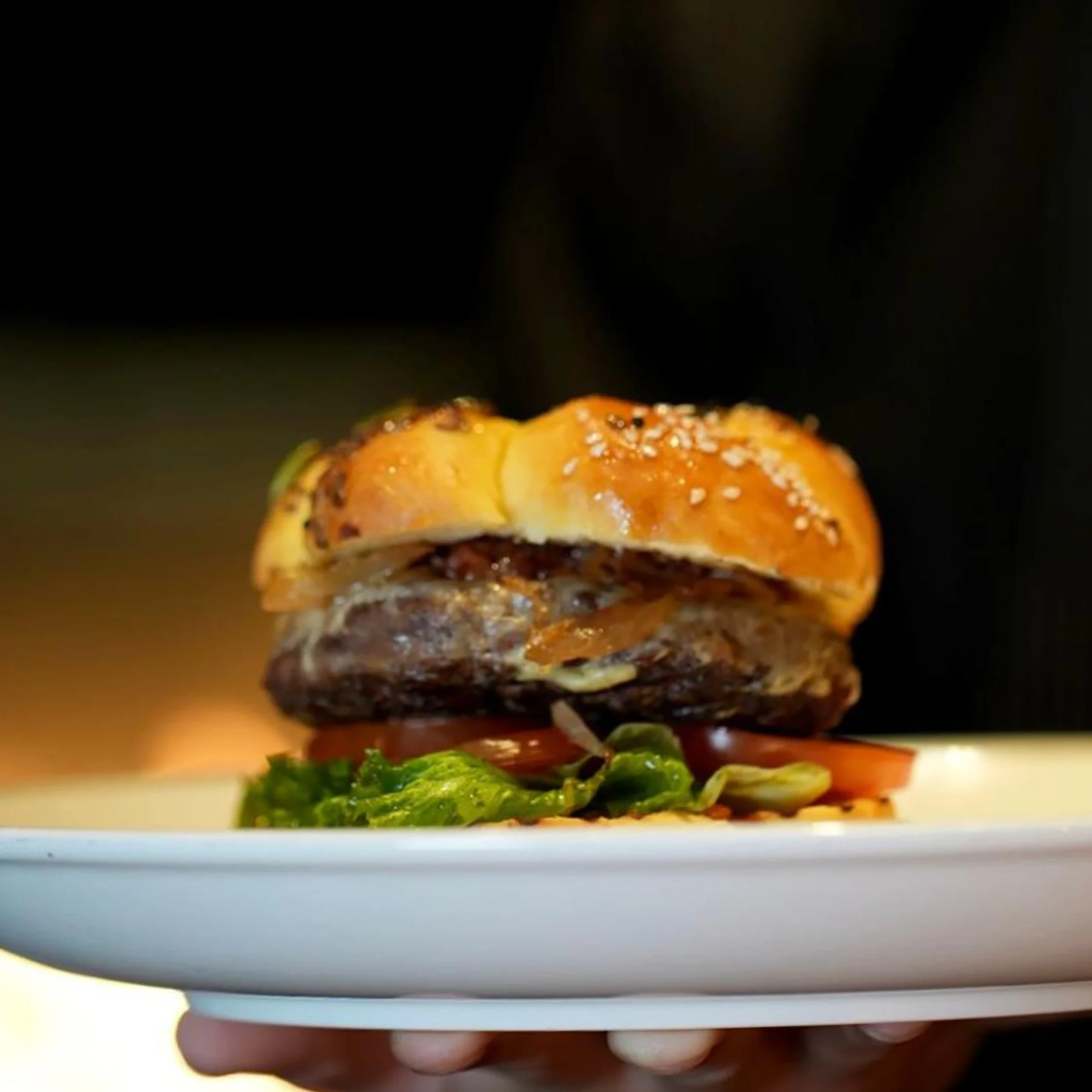 Close-up of a sesame-seed burger stacked with beef patty, lettuce and tomato on a plate.