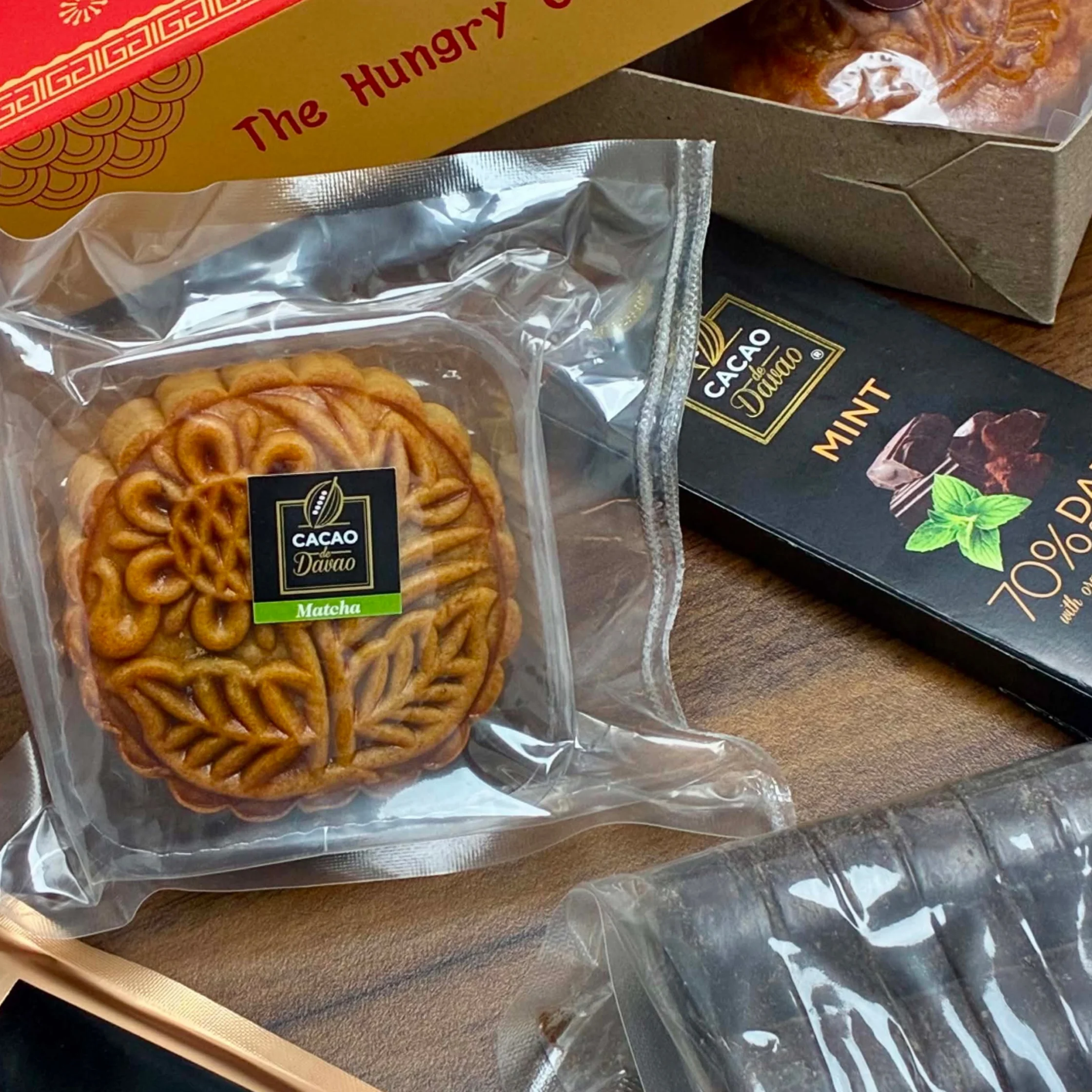 Packaged golden pastry labeled “Cacao Diano” sits beside mint dark chocolate and festive sweets, creating an appetizing holiday gift display.