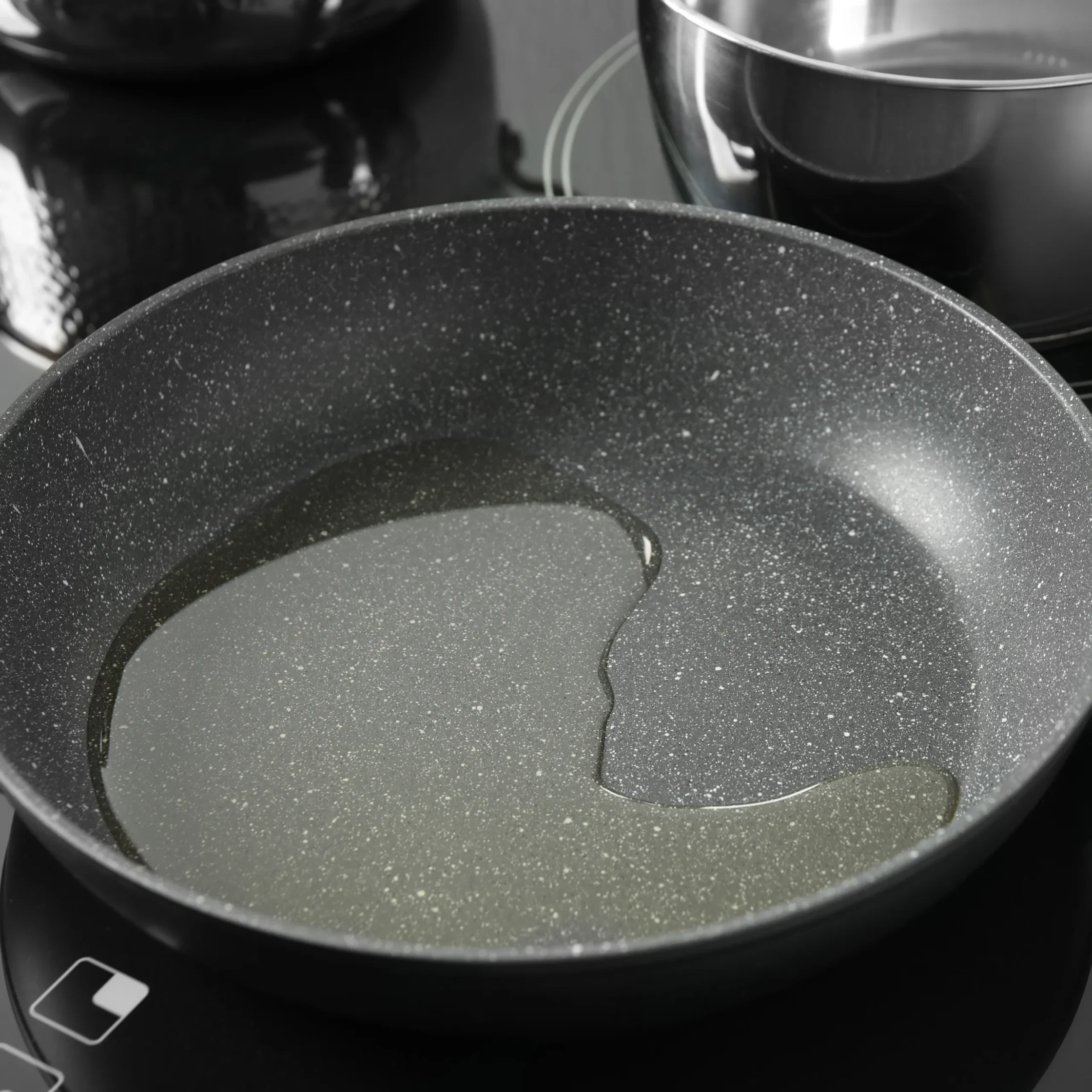 Close-up of a speckled nonstick frying pan with another pan visible in the blurred background.
