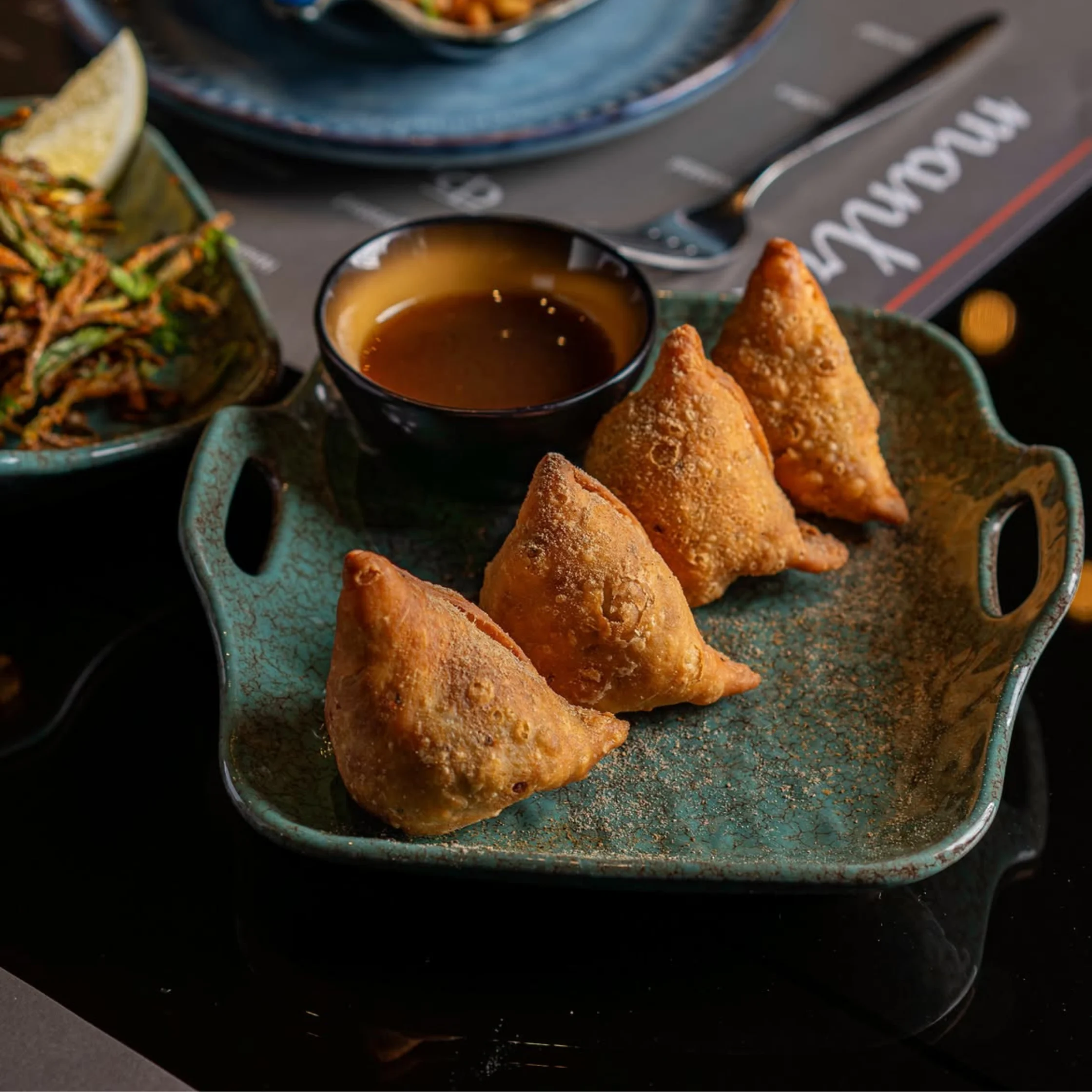 samosas from mantra served with a sauce on a beautiful teal plate