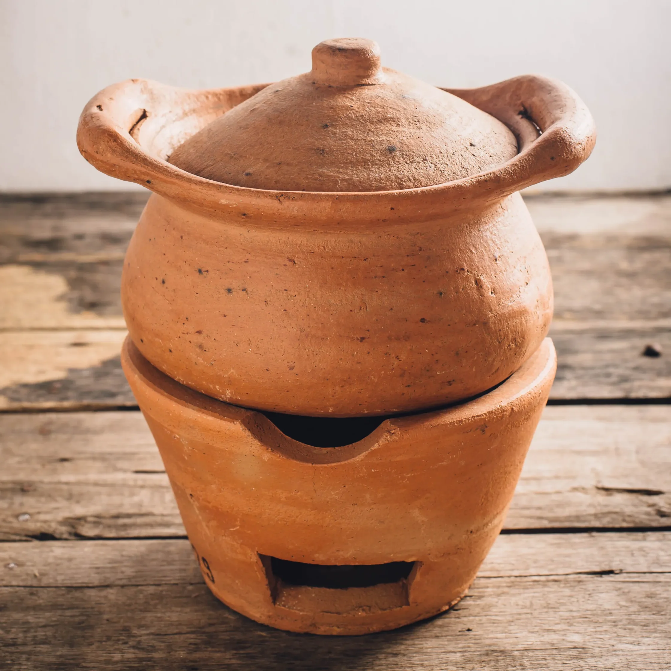 Close-up of a terracotta pot with a rounded lid on a wooden surface.