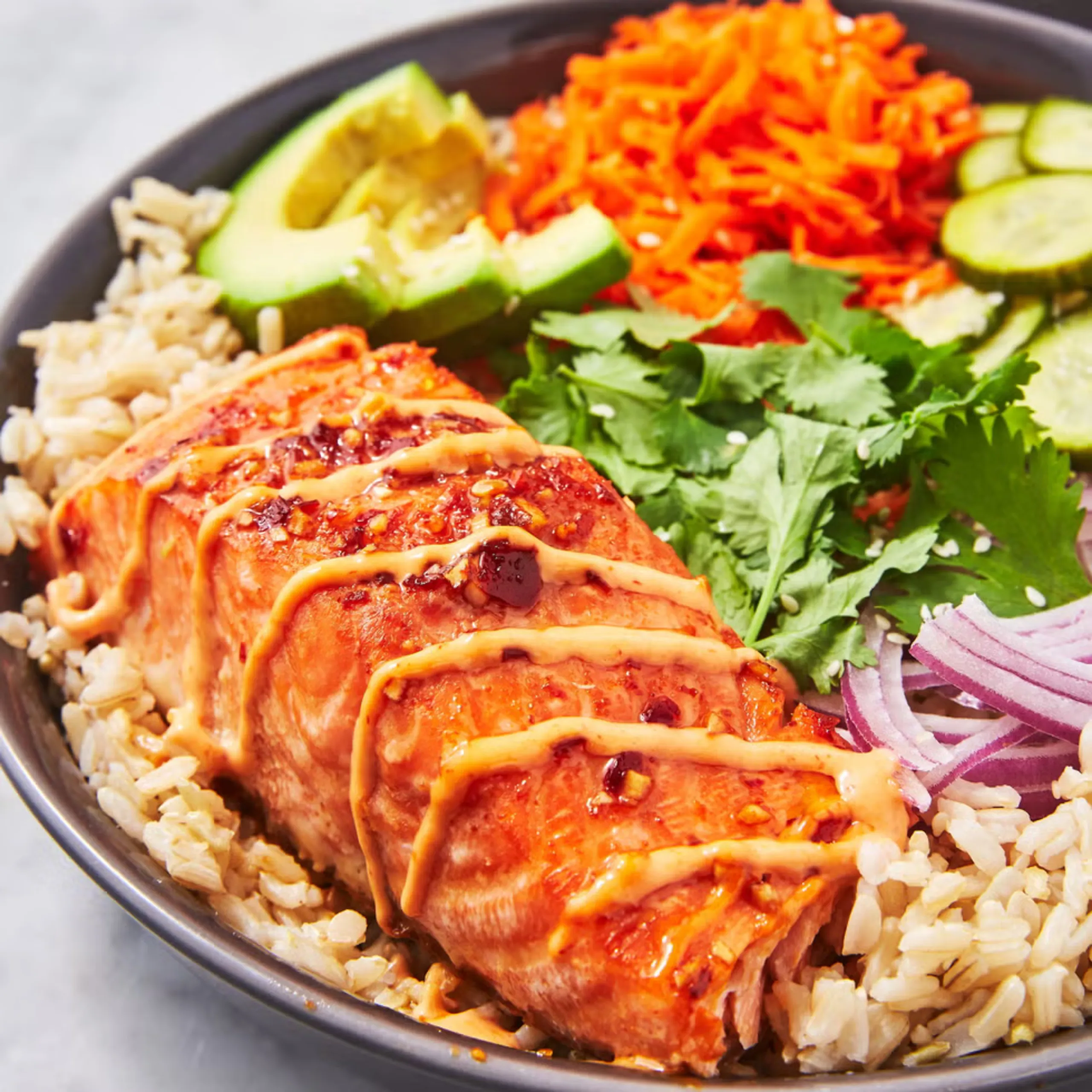 Bright burrito bowl with grilled chicken, white rice, avocado slices, shredded carrot, cucumber, and cilantro.