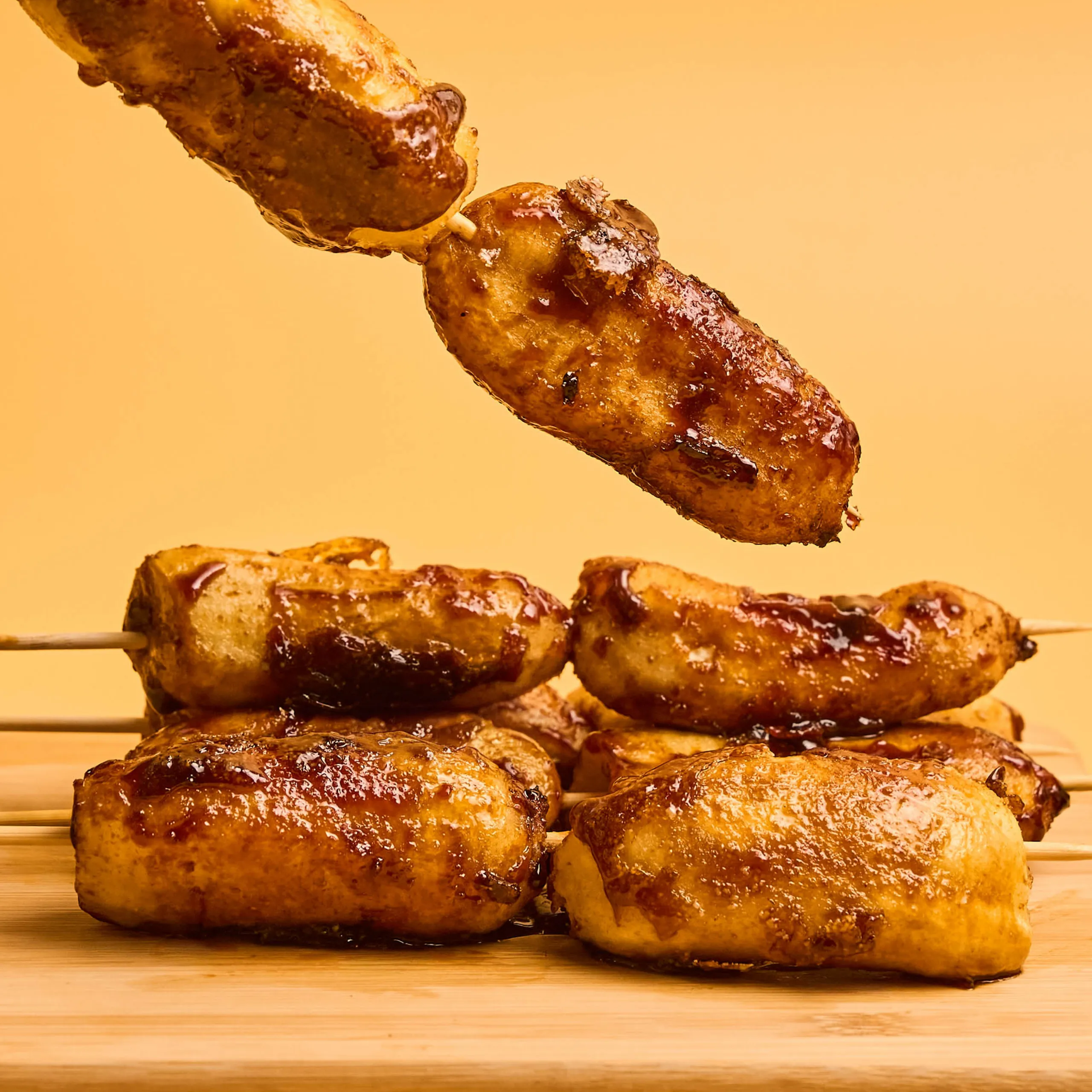 Grilled sausages on skewers stacked on a wooden surface against an orange background.