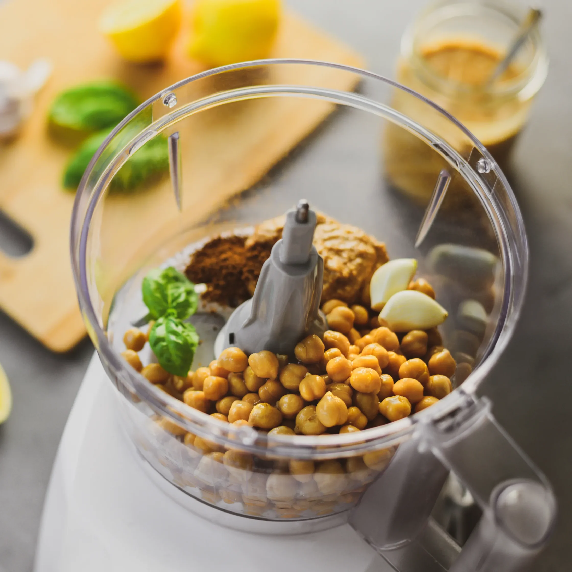 Overhead view of a food processor bowl filled with chunky green salsa, surrounded by tomatoes, cucumber, avocado, parsley, lime, and peppers.