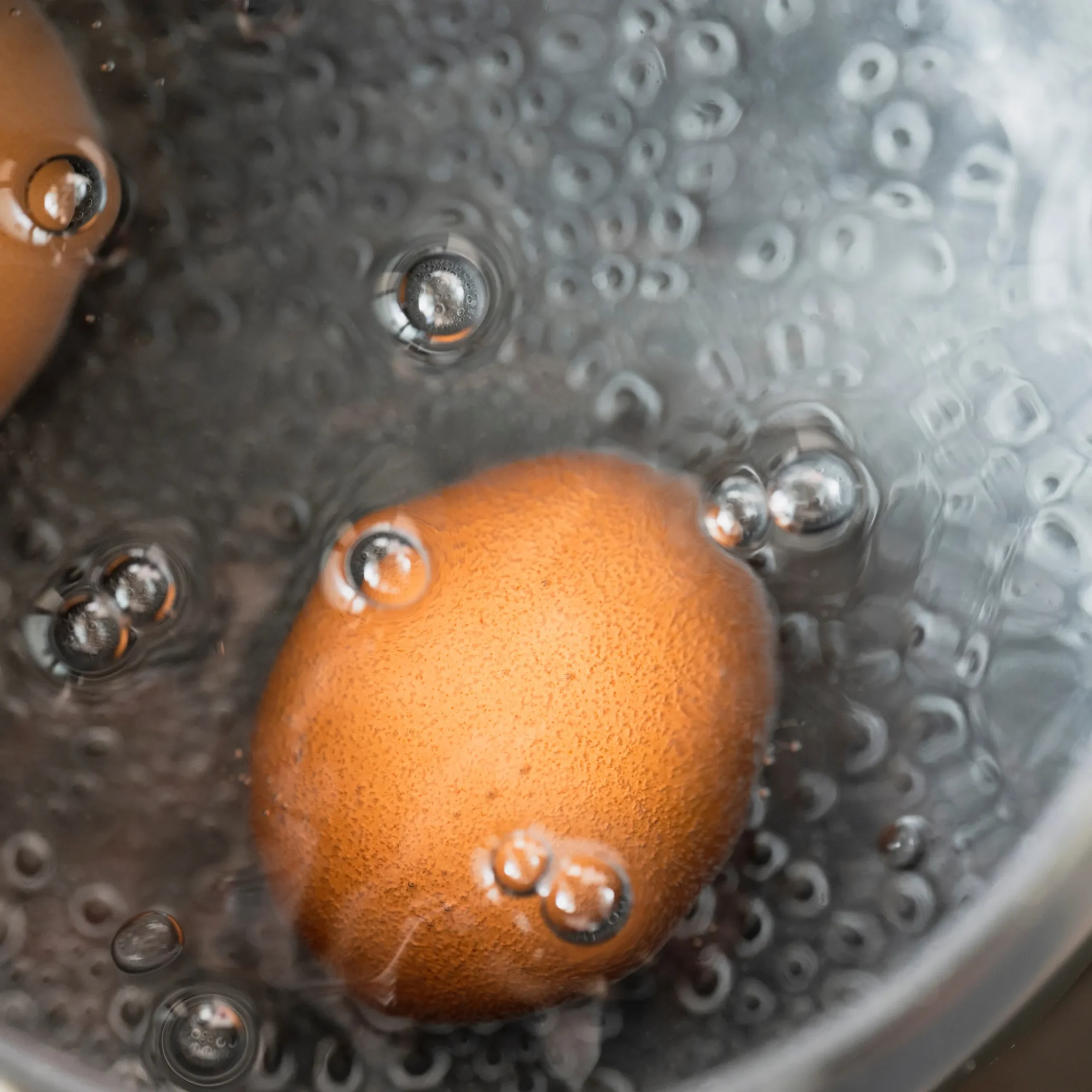 Close-up of an orange-looking fruit (peel and flesh) submerged in bubbling water, as if boiling or steaming.