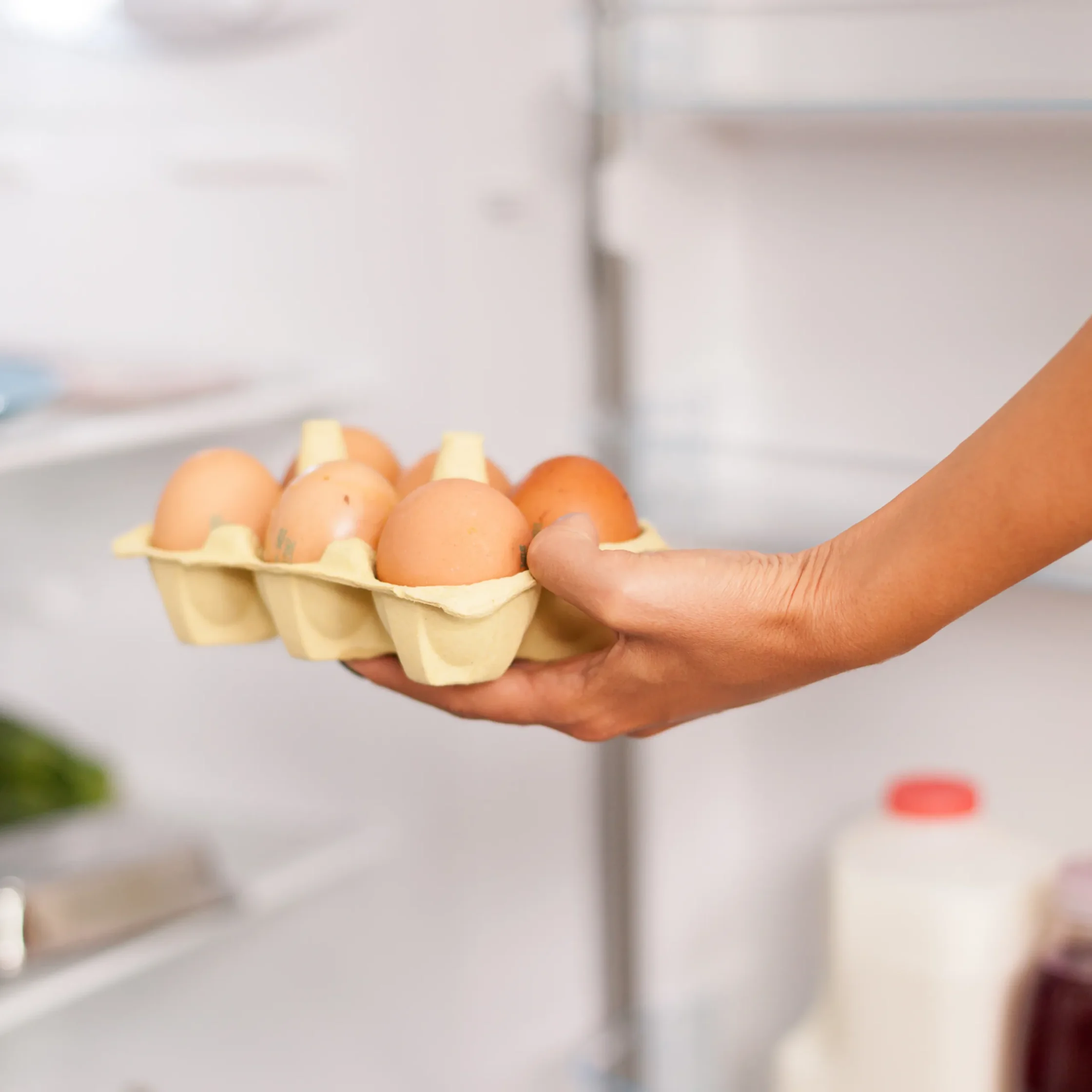 Person holding a carton of brown eggs in a kitchen setting.