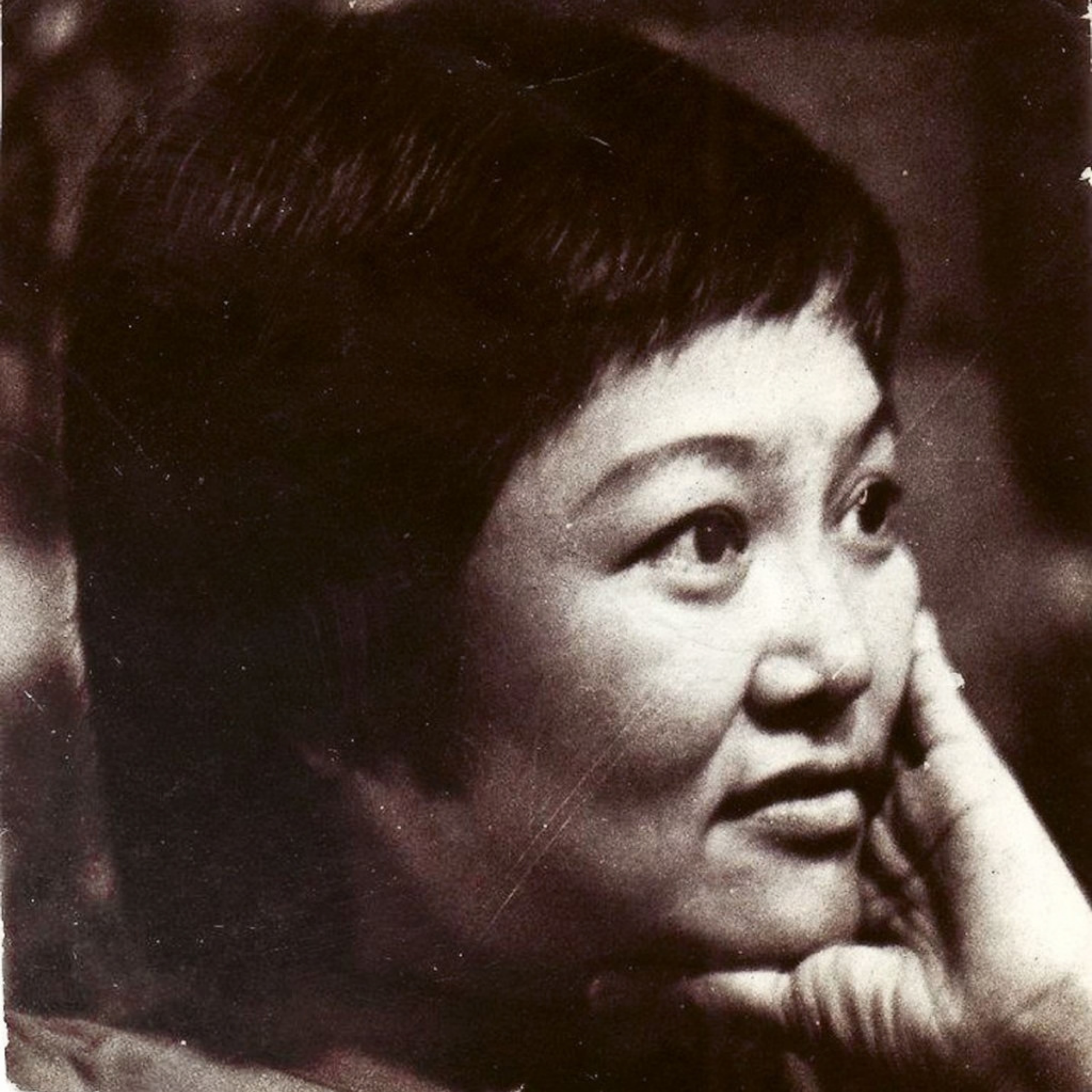 A grainy black-and-white close-up portrait shows a woman gazing upward, her cheek resting on her hand; her thoughtful expression feels gentle and reflective.
