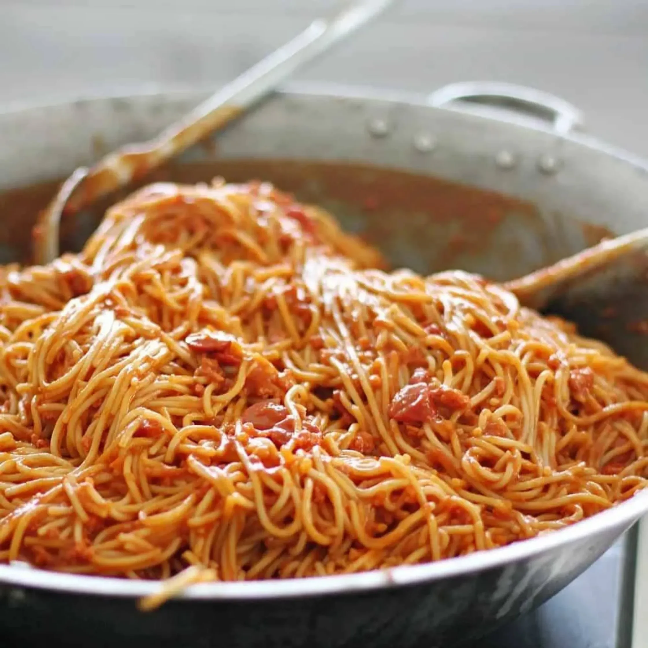 Large pan of spaghetti tossed in rich red tomato sauce, with tender noodles and tomato pieces glistening; warm, hearty, appetizing scene.