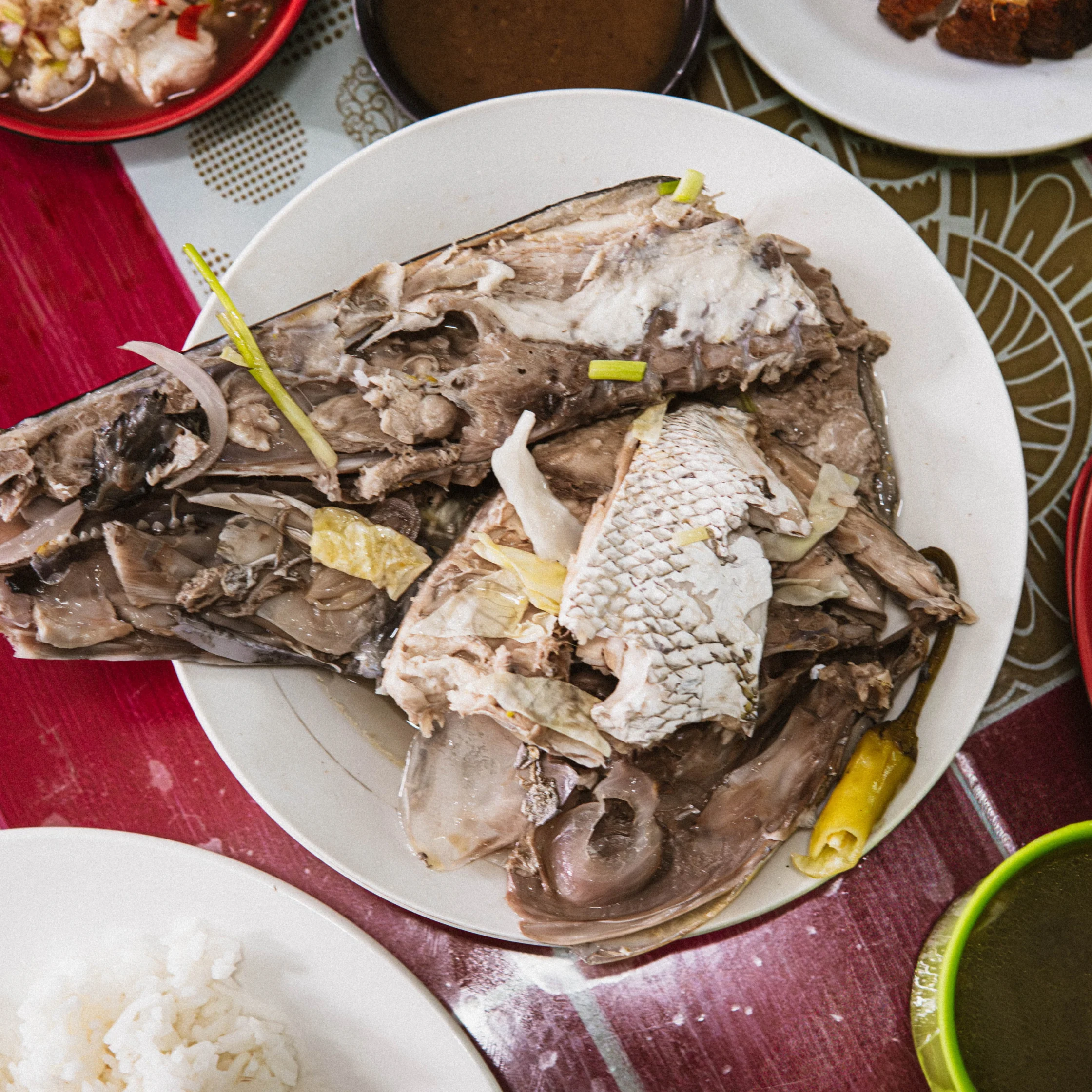 Plate with shredded fish and bones, rice on the side, and vegetable garnishes on a red tablecloth.