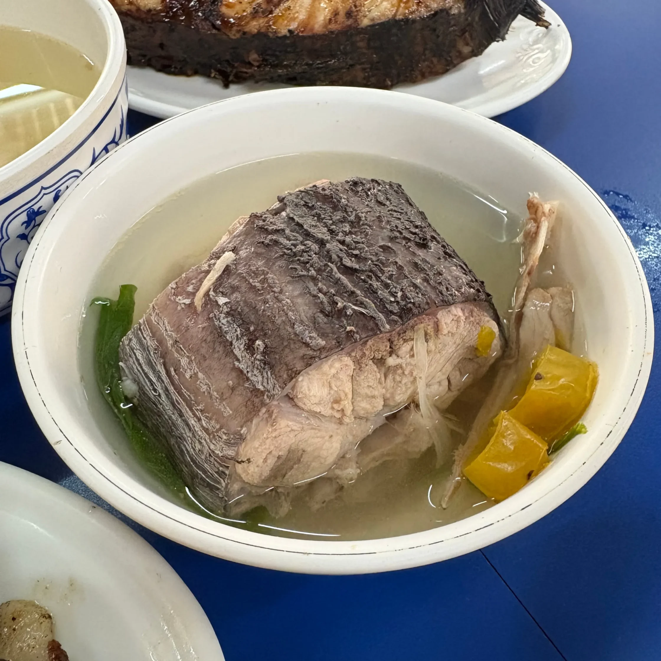 Close-up of a bowl with shredded beef in light broth and scattered vegetables on a blue table.