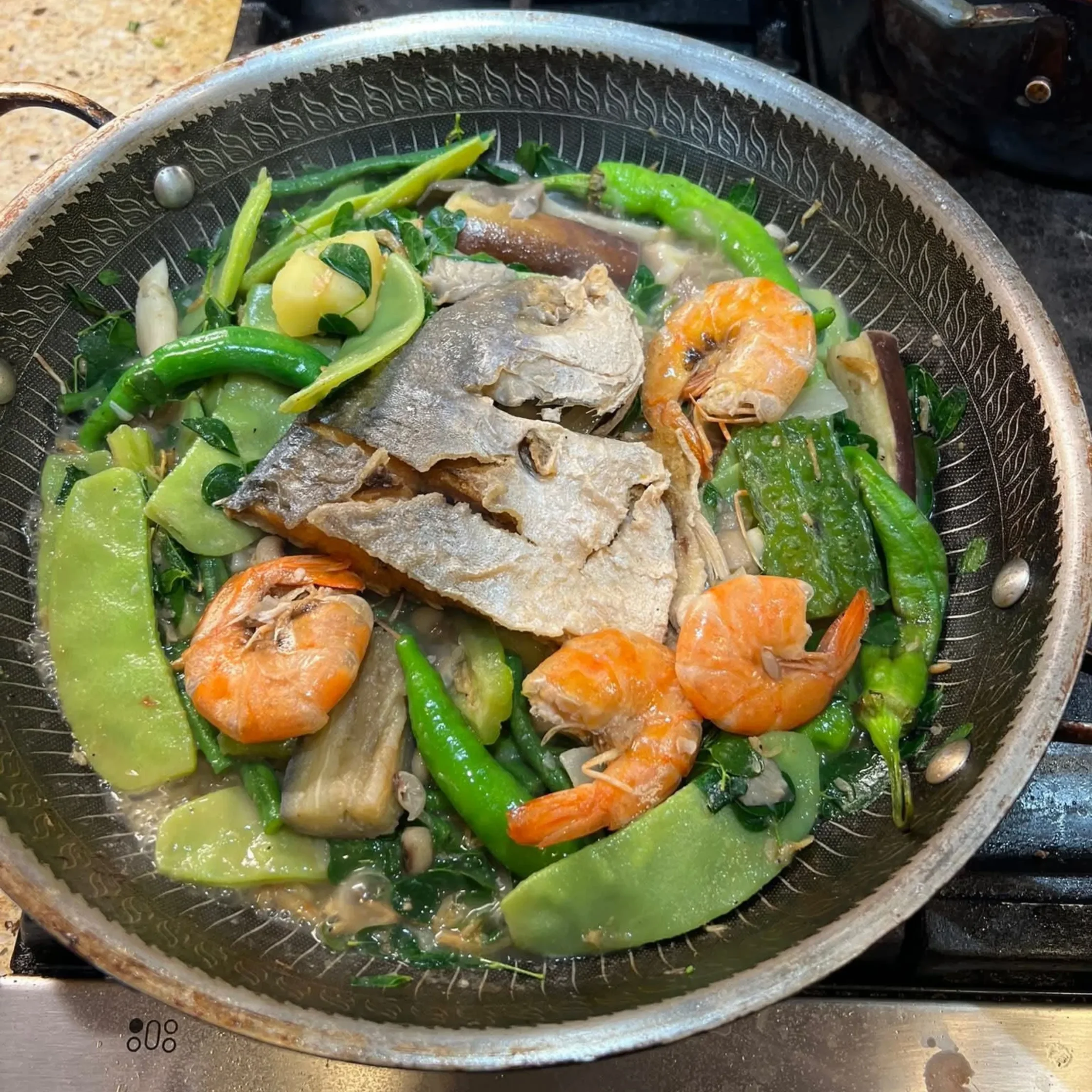 green vegetables with shrimp cooked in a dark grey pan on a stove