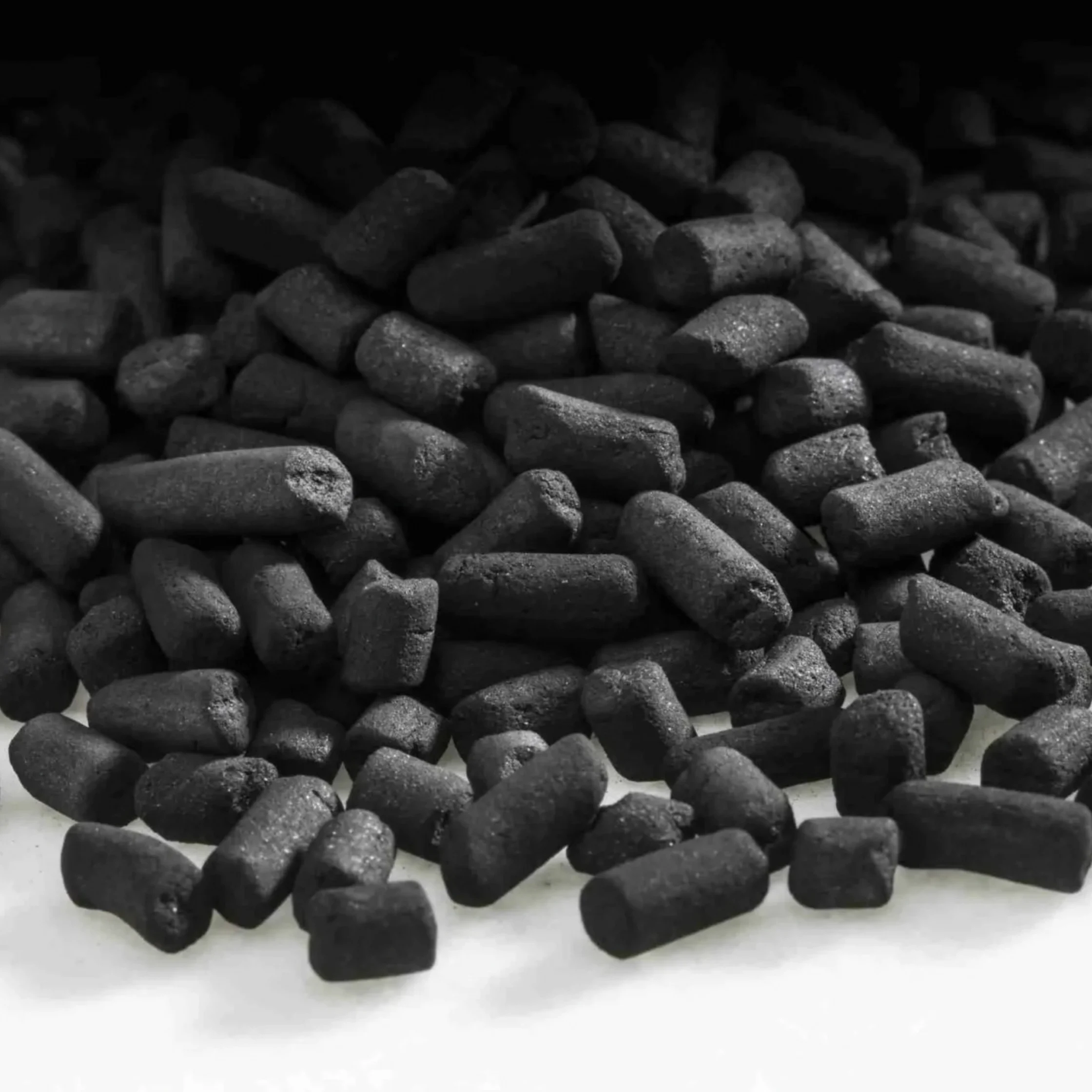 A dense pile of small, matte-black cylindrical pellets scattered across a white surface, shown in monochrome; the simple close-up feels stark and industrial.