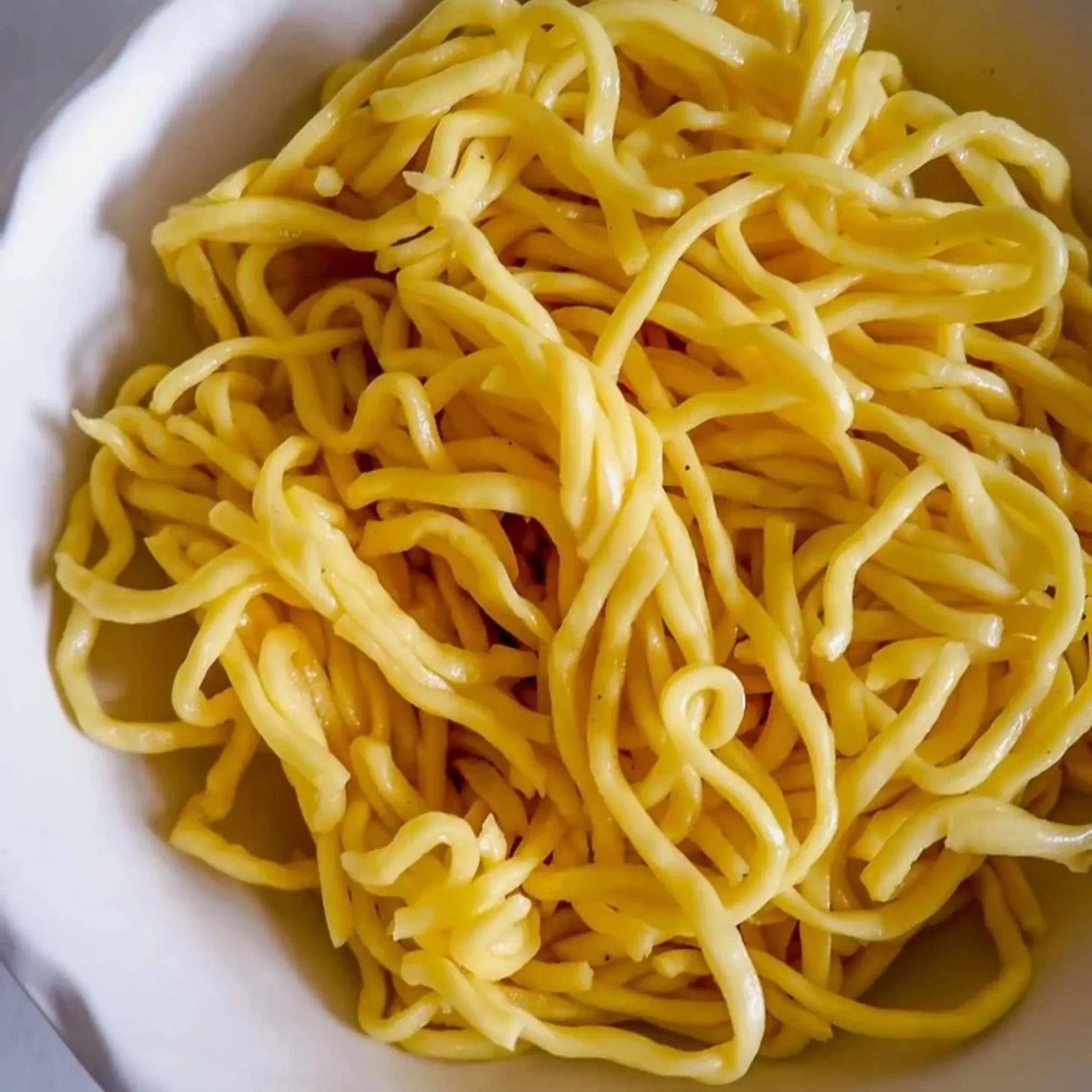 Cooked yellow pasta strands in a bowl, close-up view showing glossy surface and intertwined noodles.