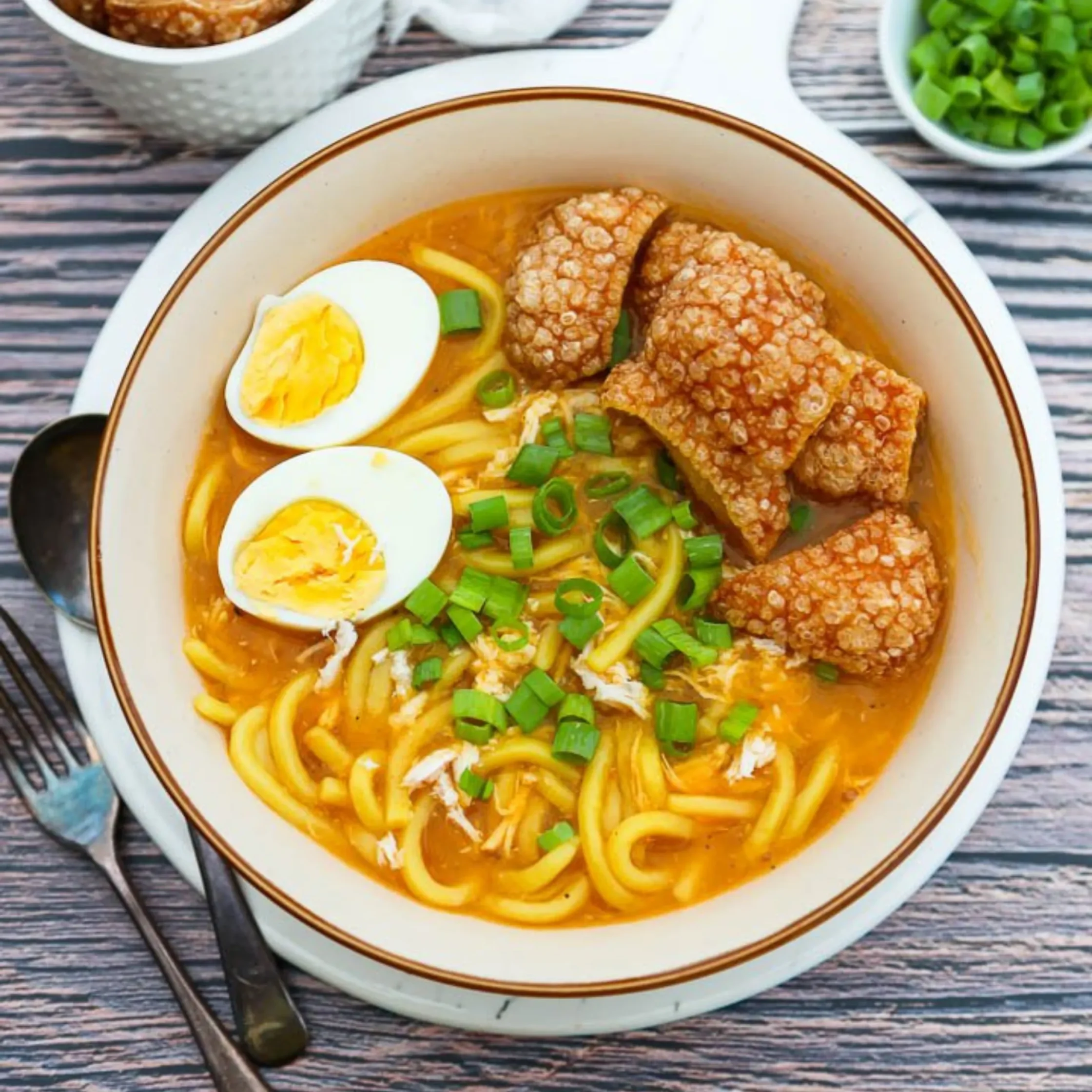 Bowl of ramen with egg halves, green onions, and crispy pork in a miso/tonkotsu broth on a wooden table