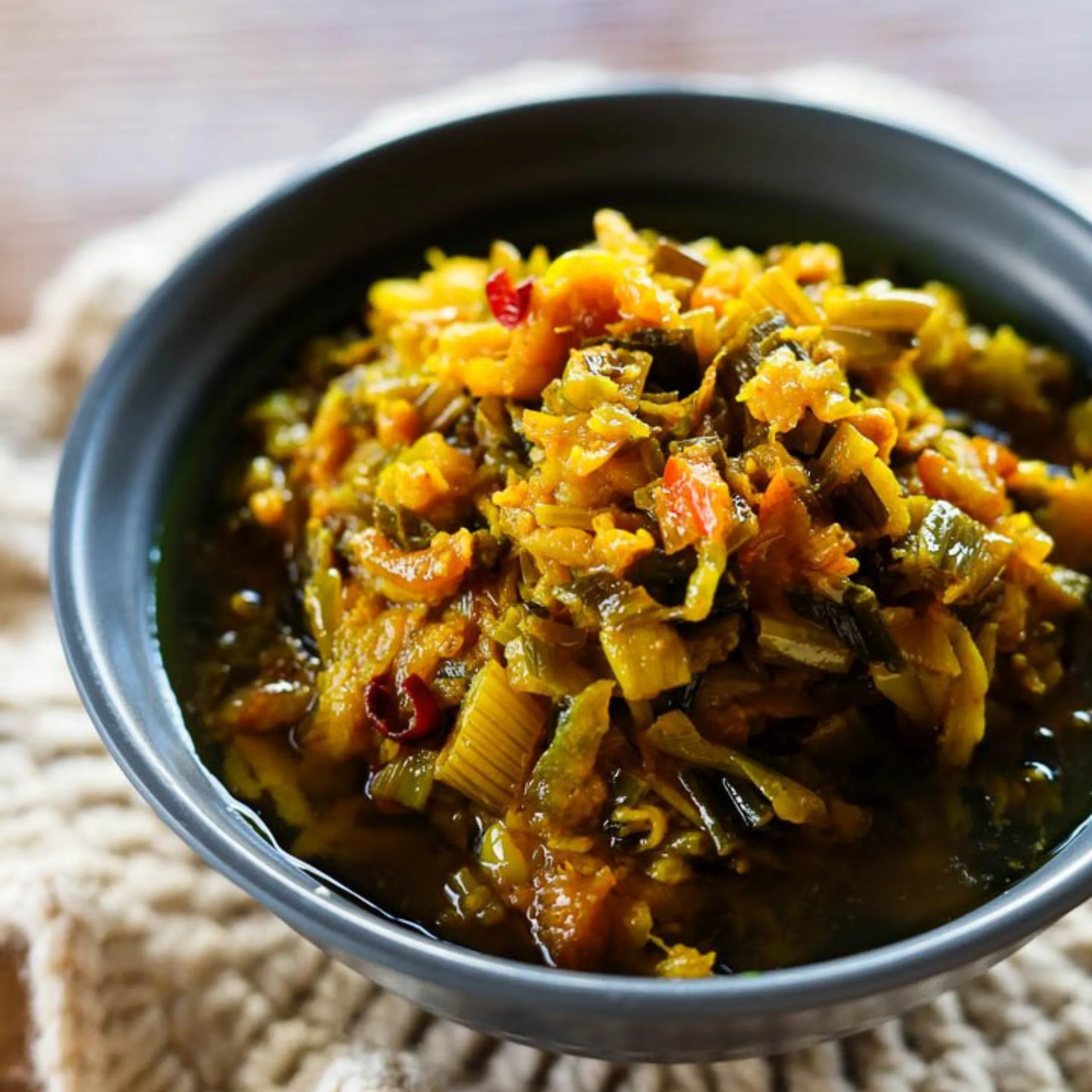Close-up of diced vegetables simmering in a dark pot, showing orange, green, and red pieces.