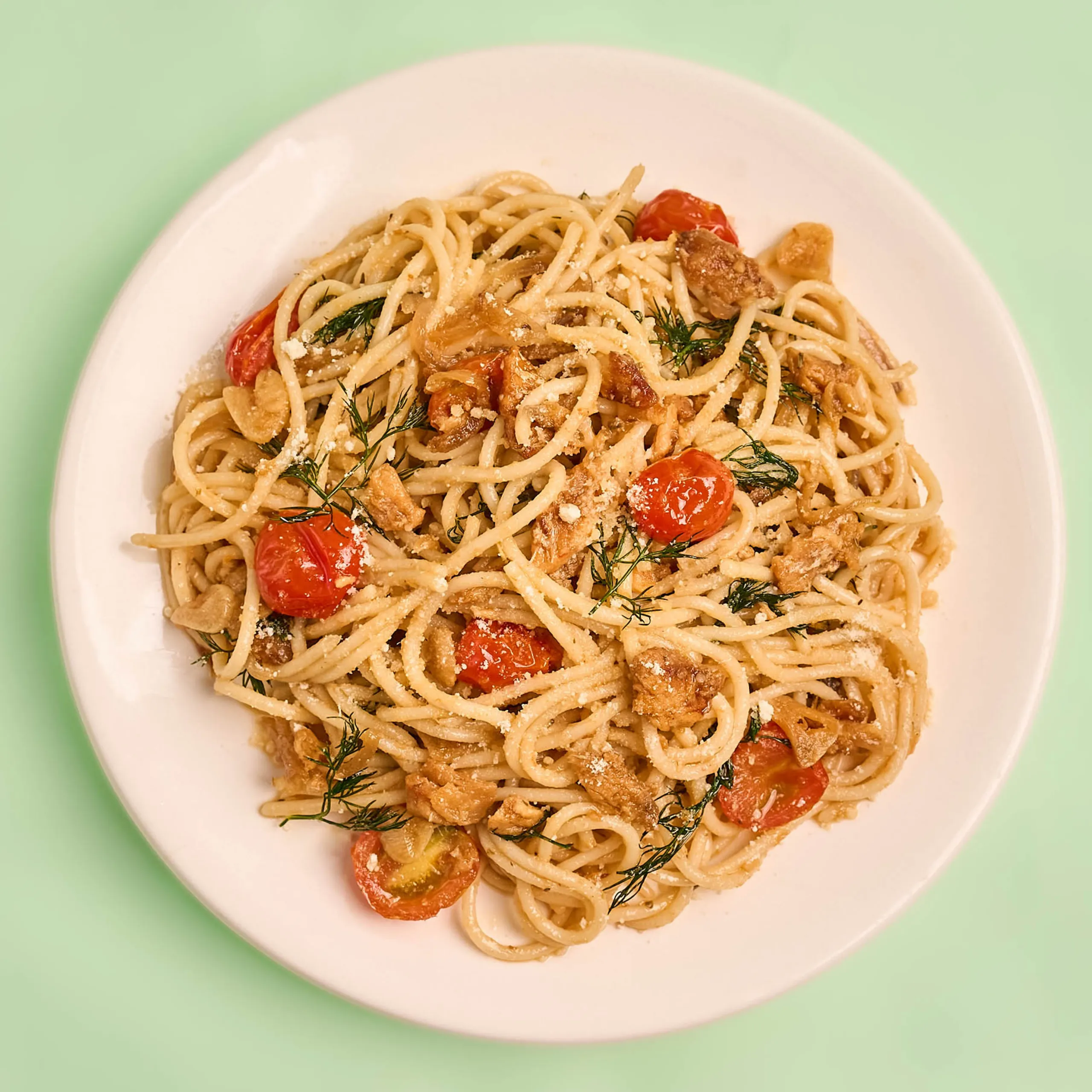 Plate of spaghetti with cherry tomatoes, grated cheese, and dill on a white dish.