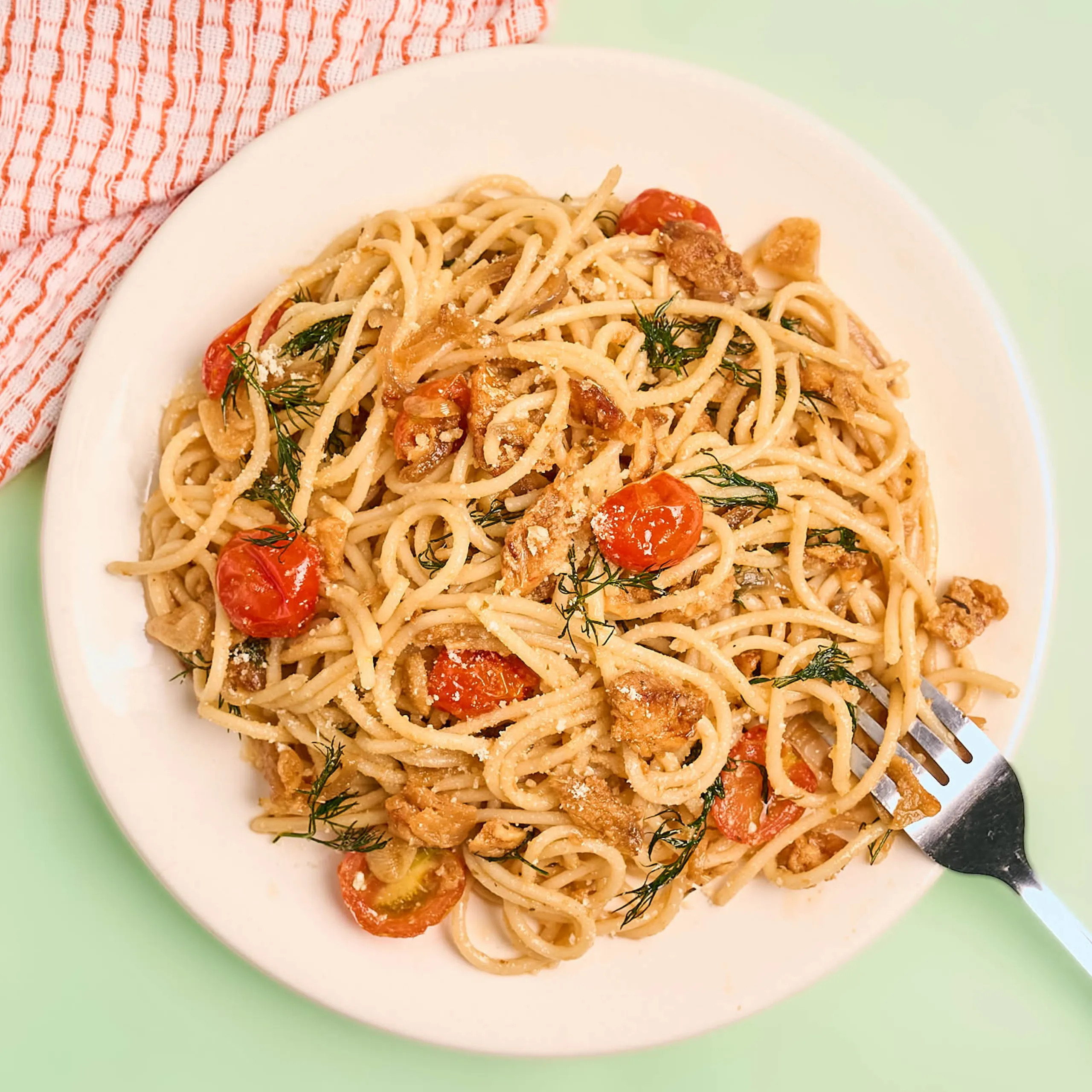 Plate of spaghetti with cherry tomatoes, dill, and grated cheese on a white dish.