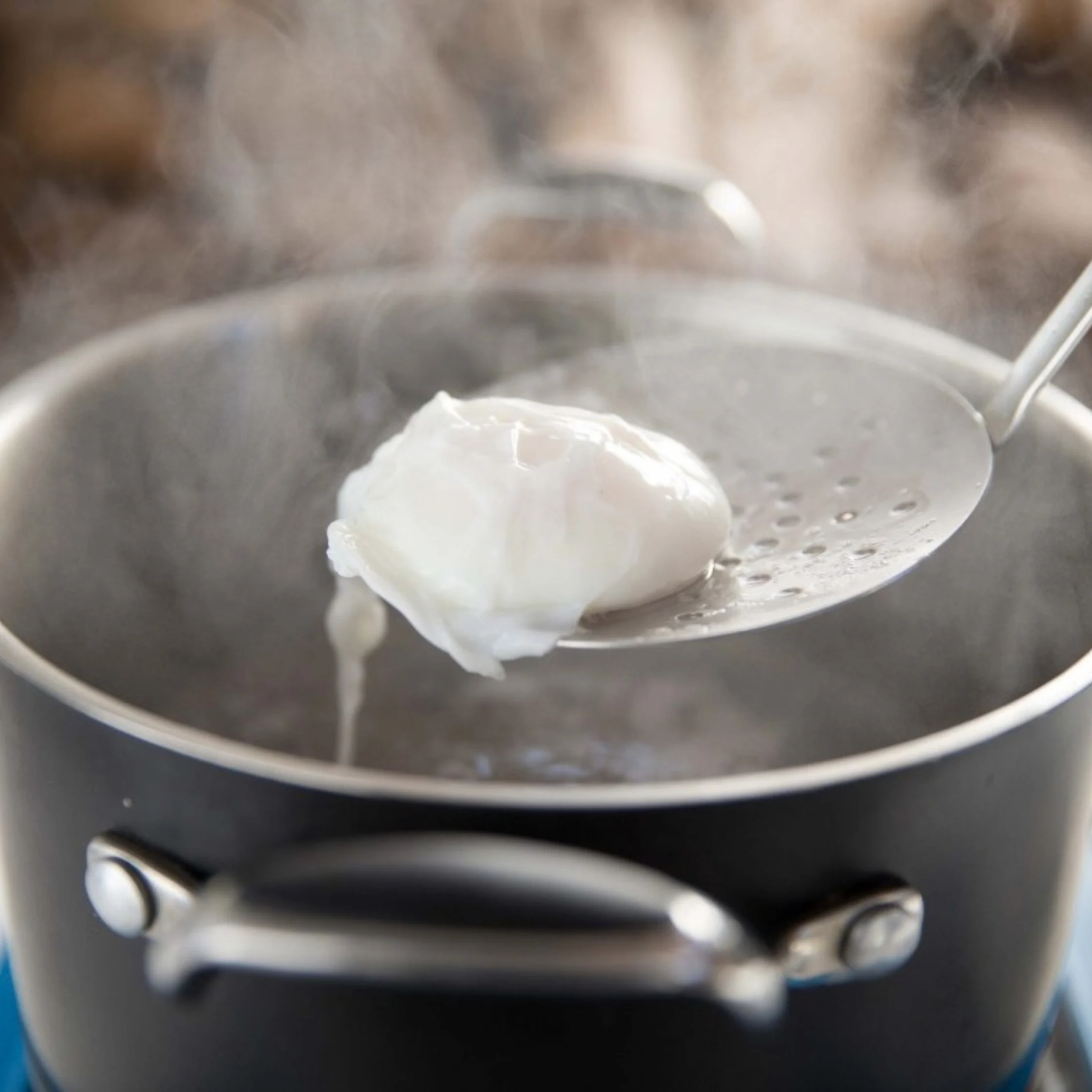 A slotted spoon lifts a soft poached egg from a steaming pot of water on a stovetop, creating a warm, calm kitchen atmosphere.