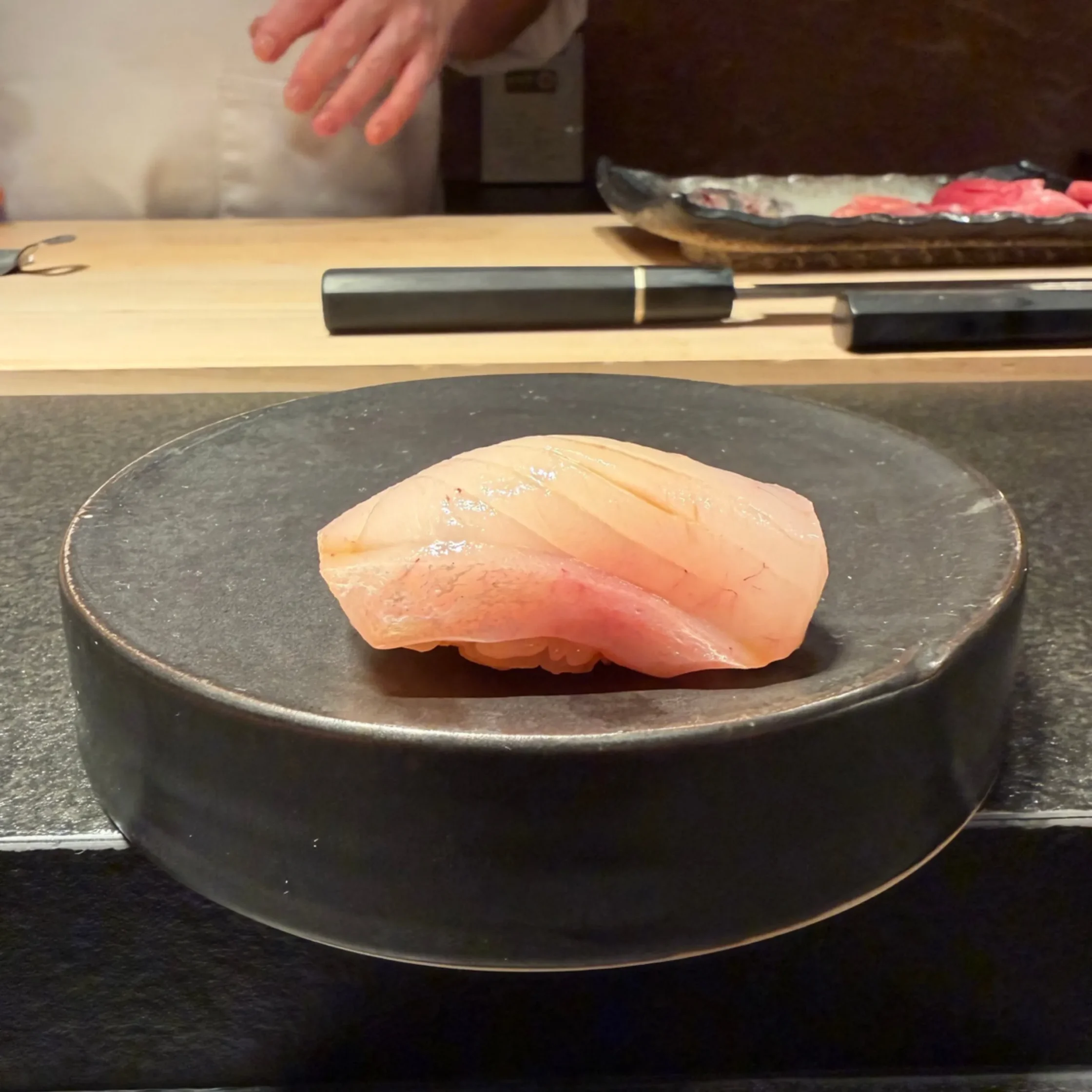 Sliced raw fish ready for sushi on a dark plate at a wooden counter