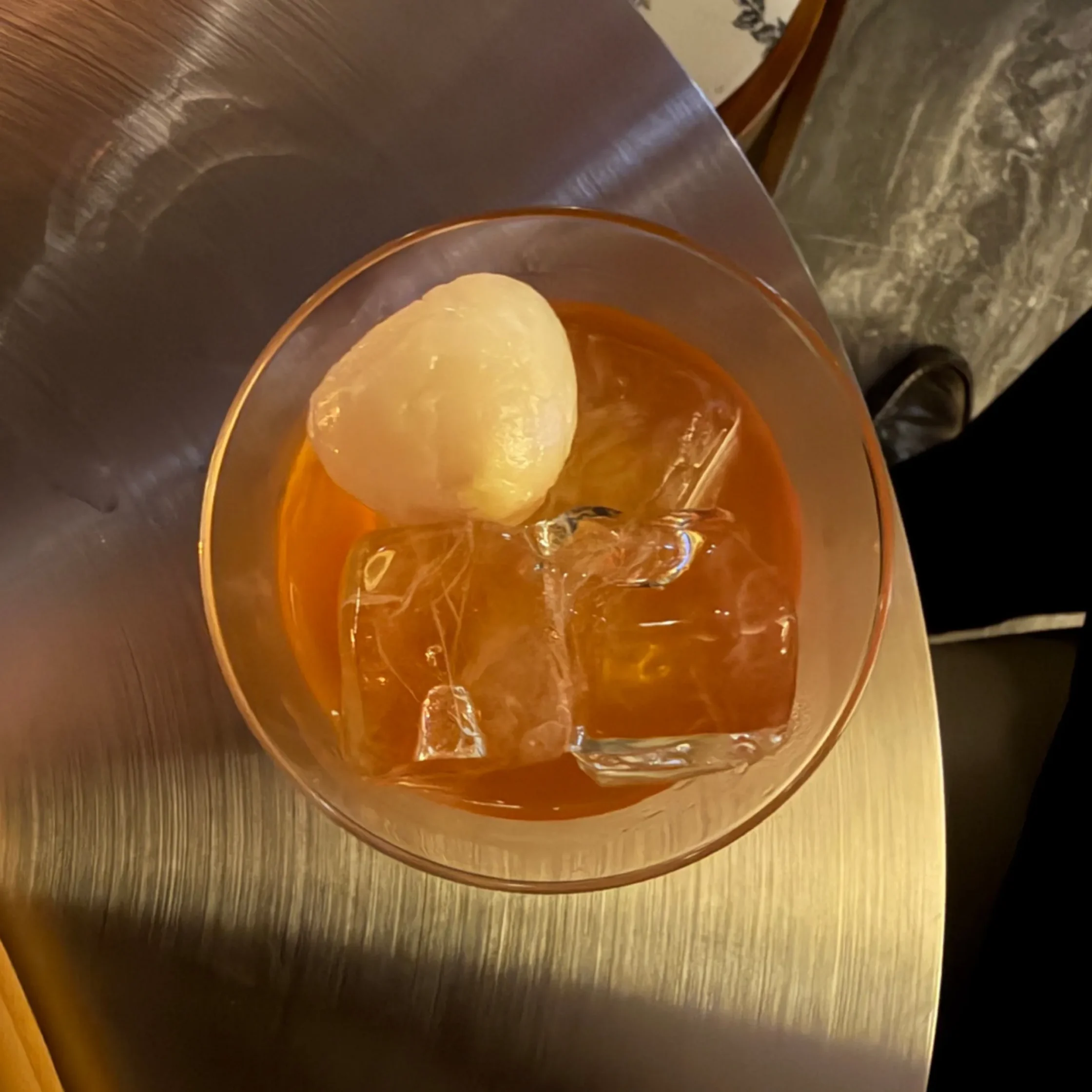Close-up of an orange drink in a stemmed glass with a lemon wheel garnish on a wood-toned surface.