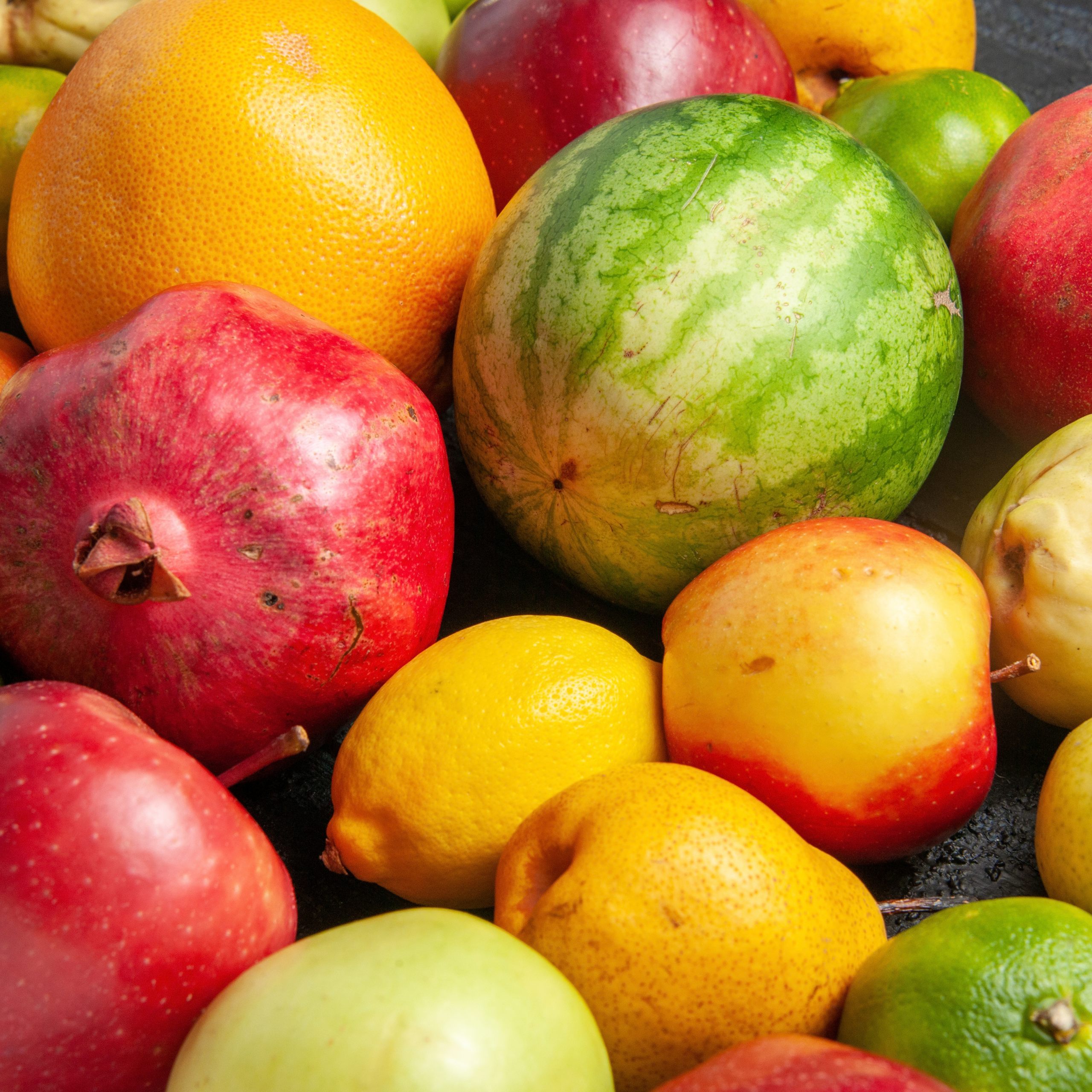 A colorful close-up of assorted fresh fruit—watermelon, oranges, pomegranates, lemons, and apples—packed together, creating a vibrant, abundant feel.