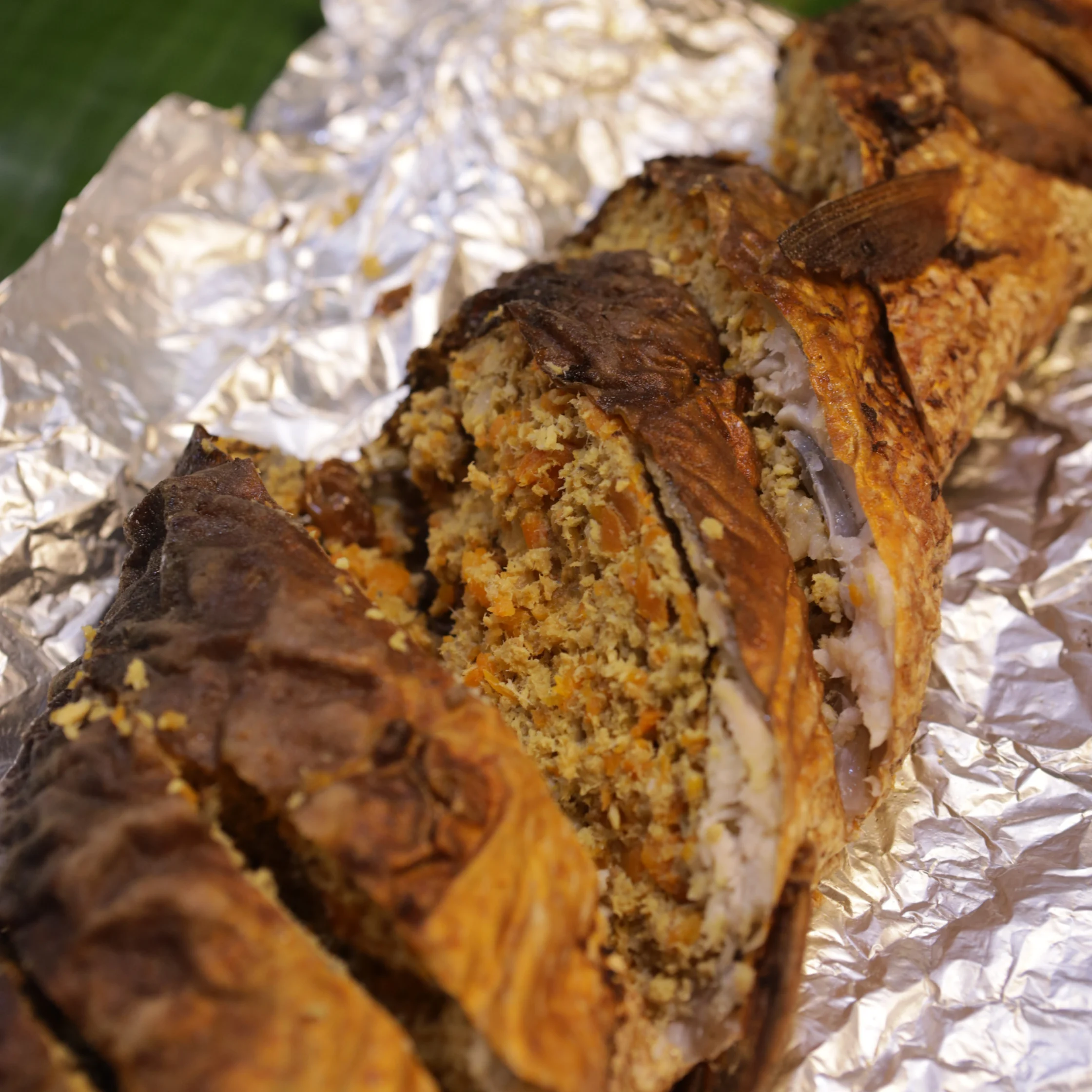 Roasted stuffed milkfish sliced open on crinkled foil, revealing golden herb-and-crumb filling beneath crisp browned skin; a hearty, rustic meal.