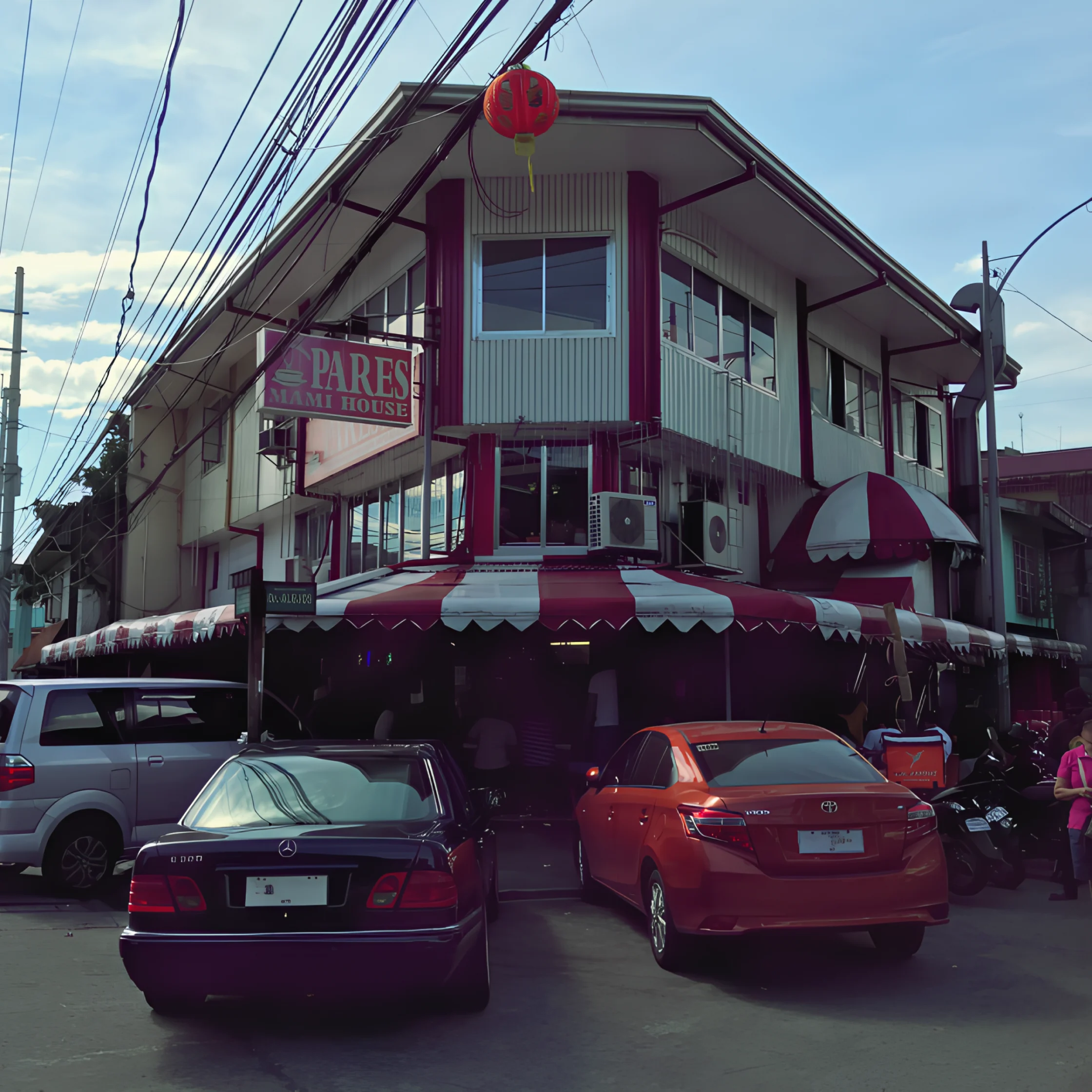 A two-story corner shop with a red lantern, striped awnings, and a “Pares” sign stands beneath tangled wires; parked cars create a busy street scene.