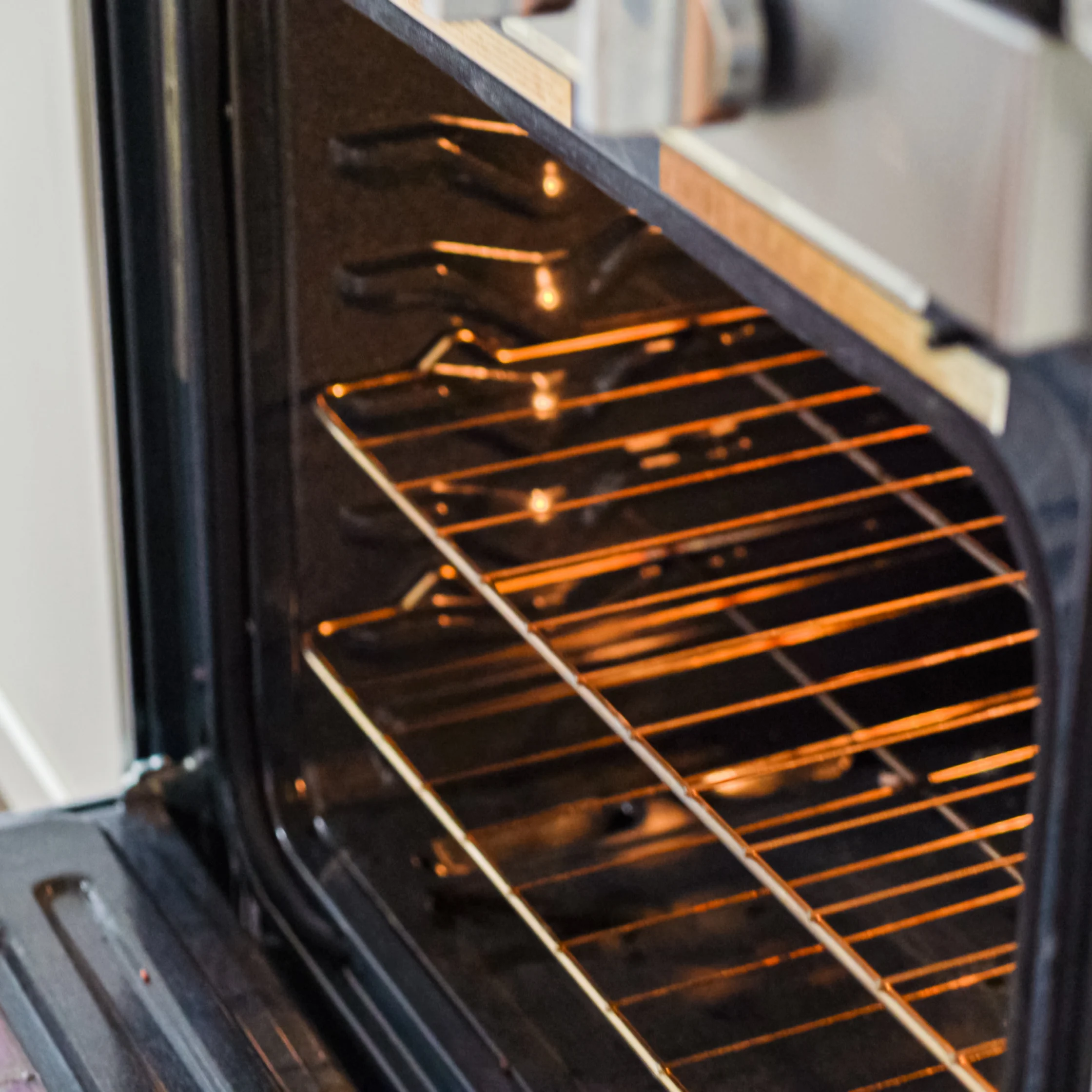 An open oven glows warmly, illuminating empty metal racks inside a clean kitchen appliance, creating a cozy, inviting atmosphere.