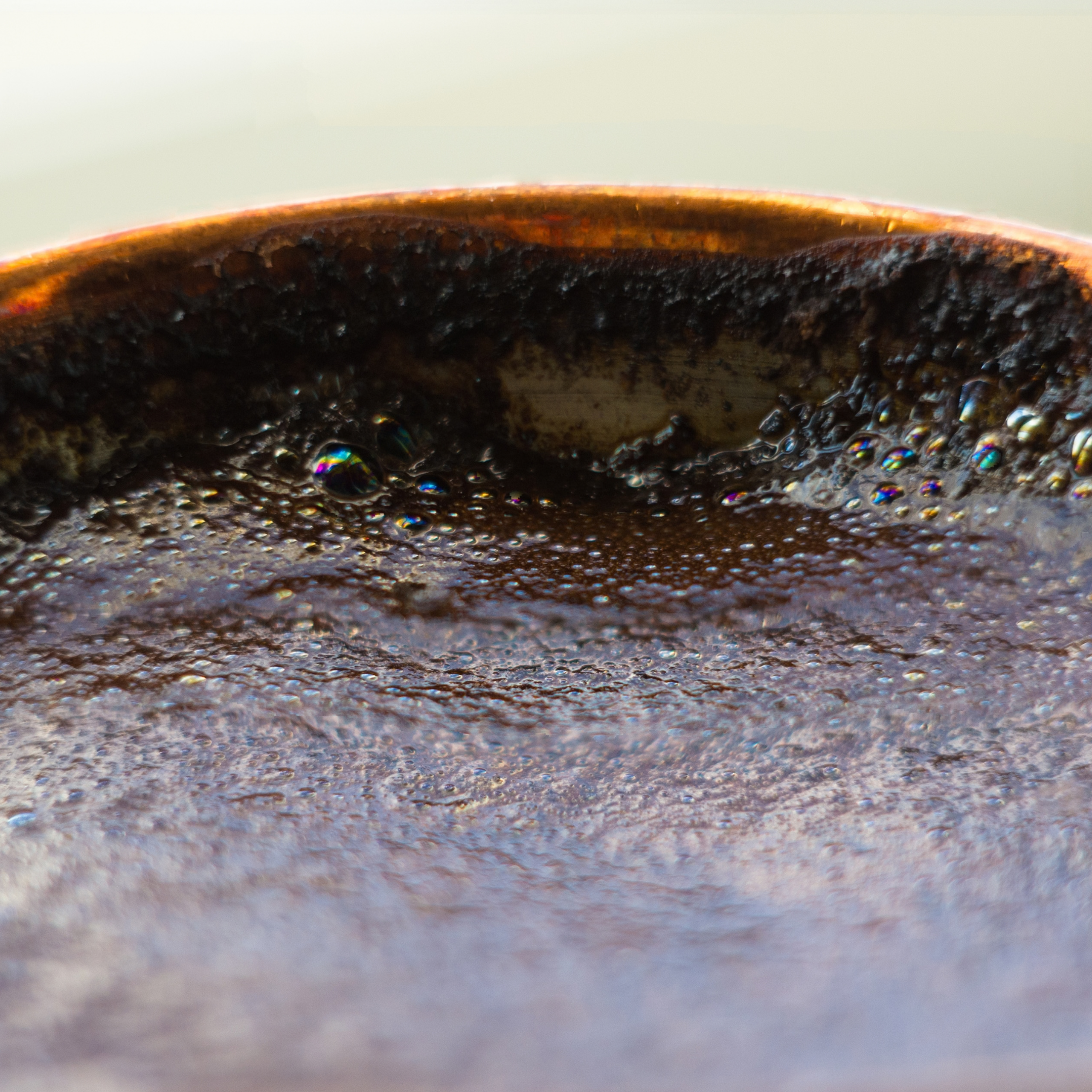 Extreme close-up of a dark, glossy liquid simmering in a pan, with tiny bubbles and an orange-lit rim; the texture feels rich and warm.