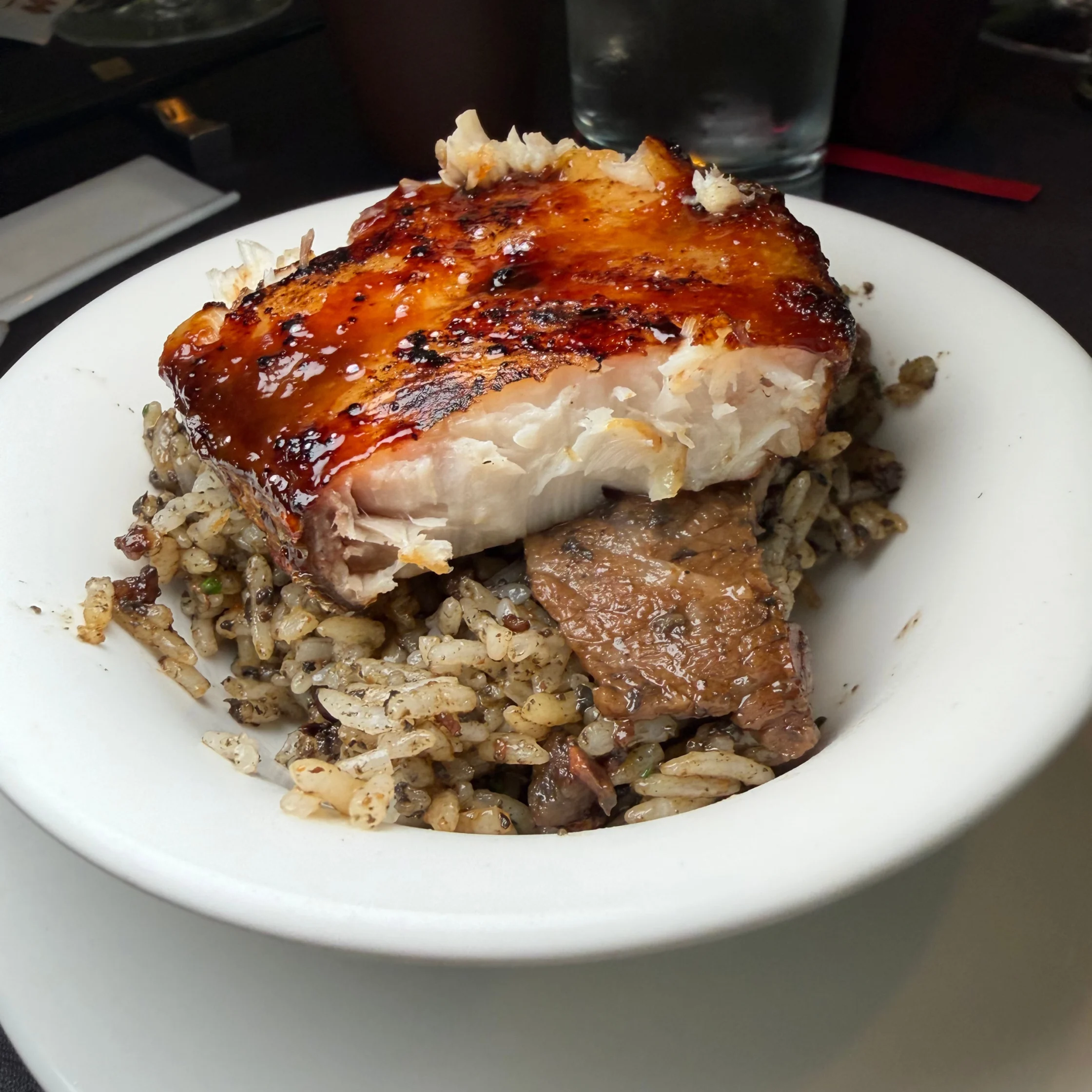 Glazed, caramelized roasted meat rests over seasoned rice in a white bowl, with a tender cutaway showing pale meat; a hearty, savory meal.