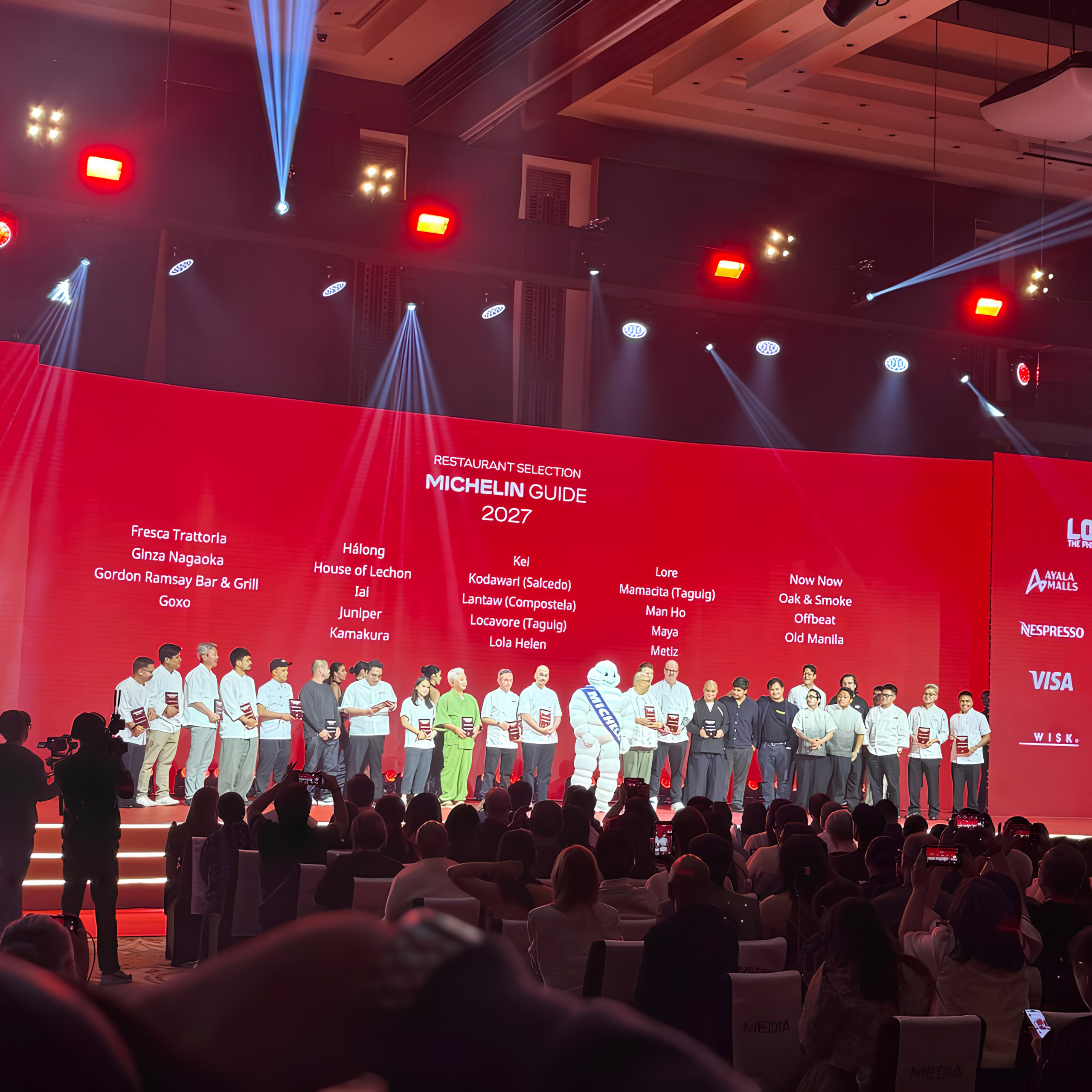 A presenter stands on a vivid red MICHELIN Guide stage at a Manila restaurant ceremony, while a seated audience watches beneath bright spotlights.