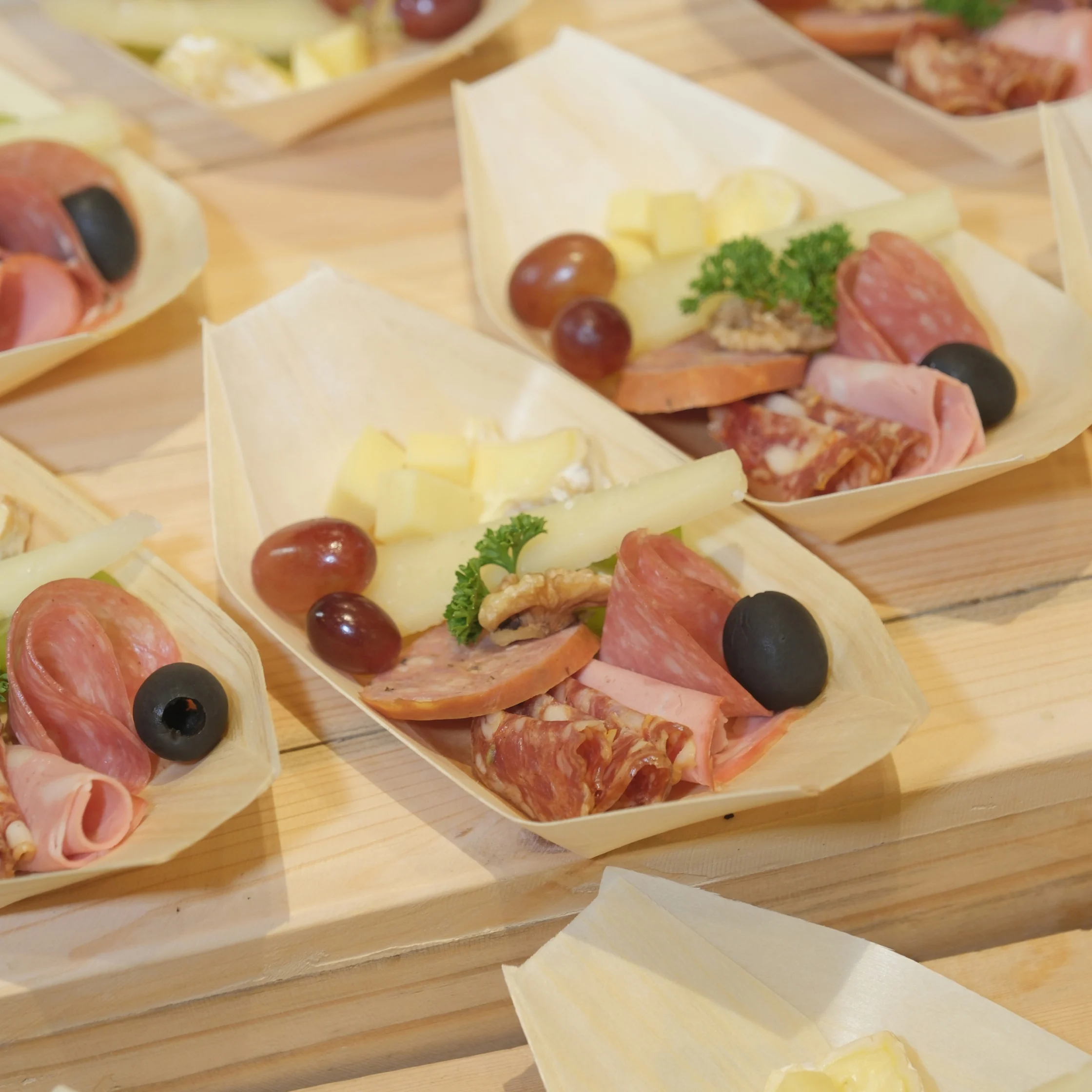 Wooden trays of assorted cured meats, sliced cheese, olives, grapes, and parsley arranged on a wooden table create an inviting, festive appetizer spread.