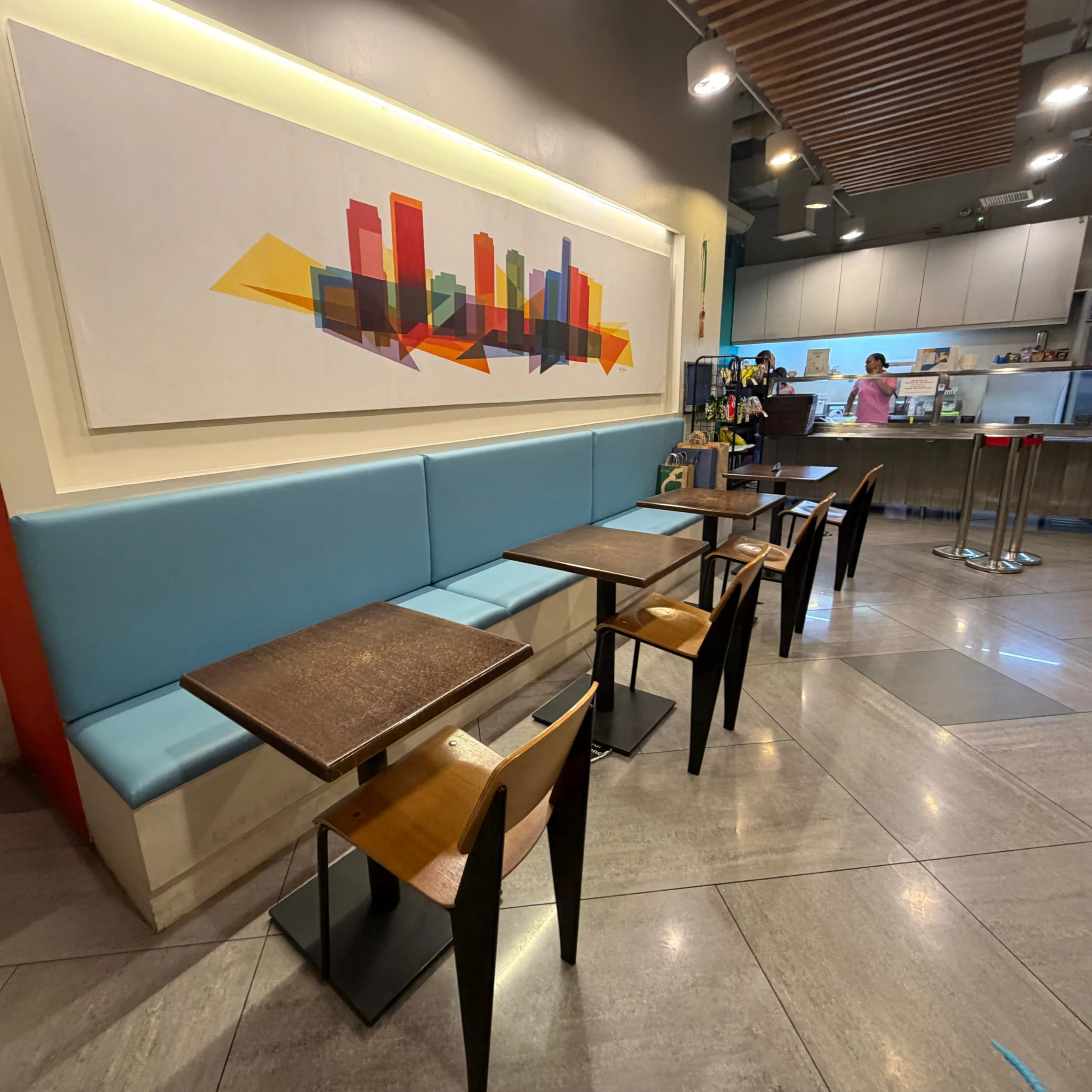 A modern café with blue booth seating, wooden tables and chairs, and colorful abstract cityscape art; warm lighting creates a calm, welcoming atmosphere.